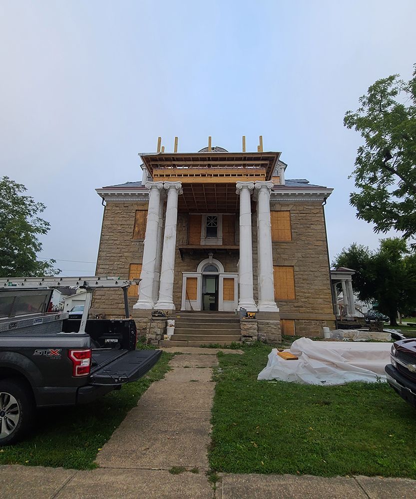 Historic house undergoing renovation with scaffolding and boarded-up windows; pickup truck in the foreground.
