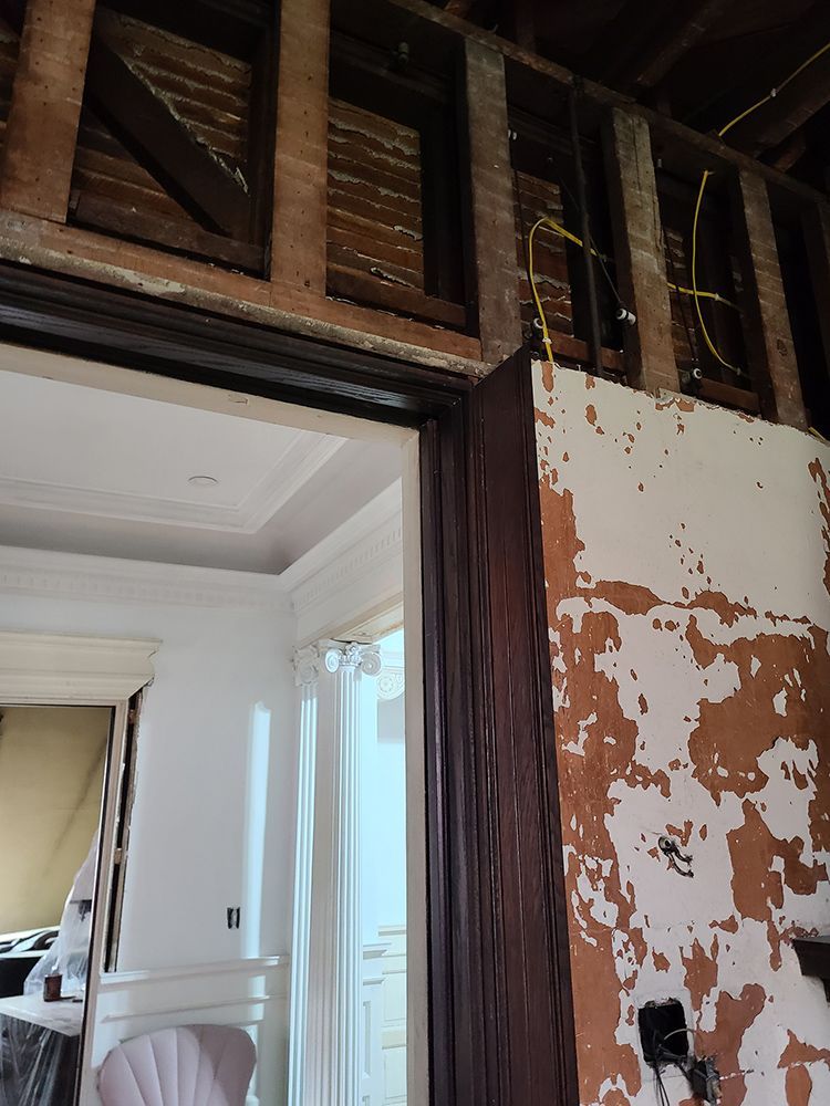 Interior view of a doorway during renovation; exposed wall studs and wiring above the frame; trim and partially painted wall.