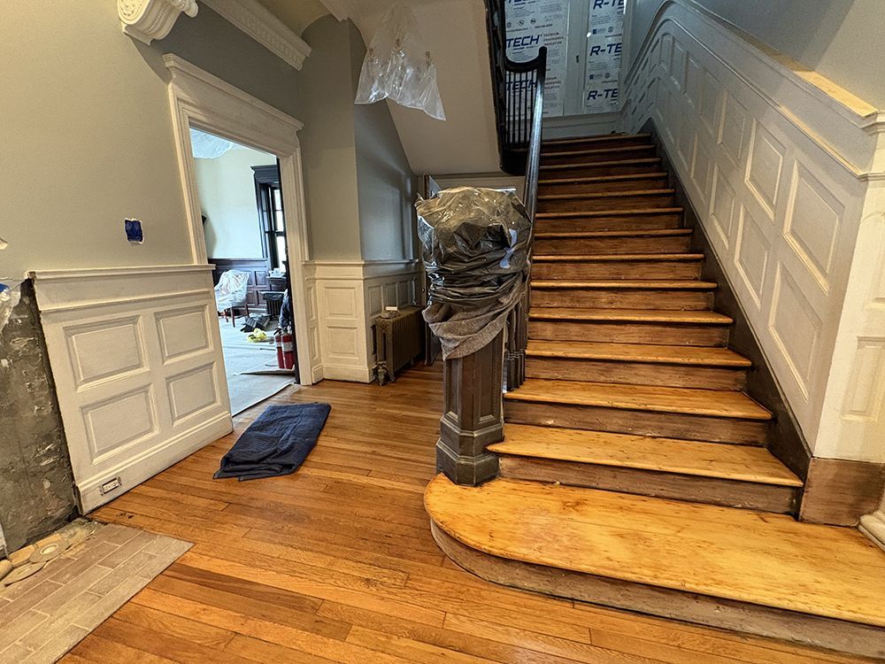 Interior hallway with wooden staircase, wood floors, and white wainscoting.
