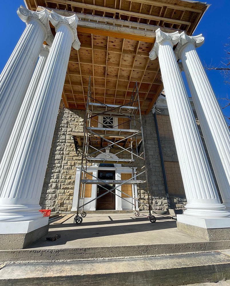 Exterior view of building with large white columns and scaffolding; construction in progress.