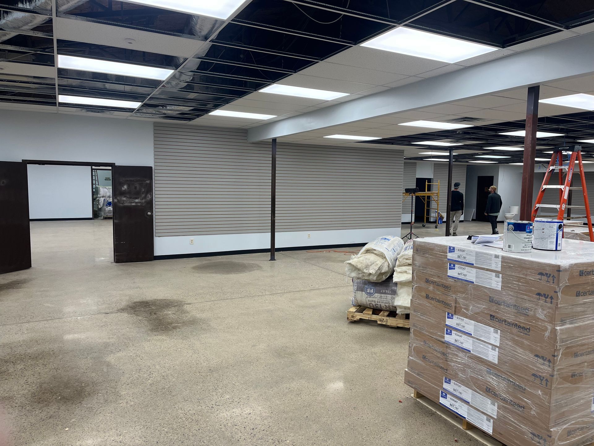 Interior construction of a commercial space with exposed ceiling, concrete floor, and pallets of supplies.