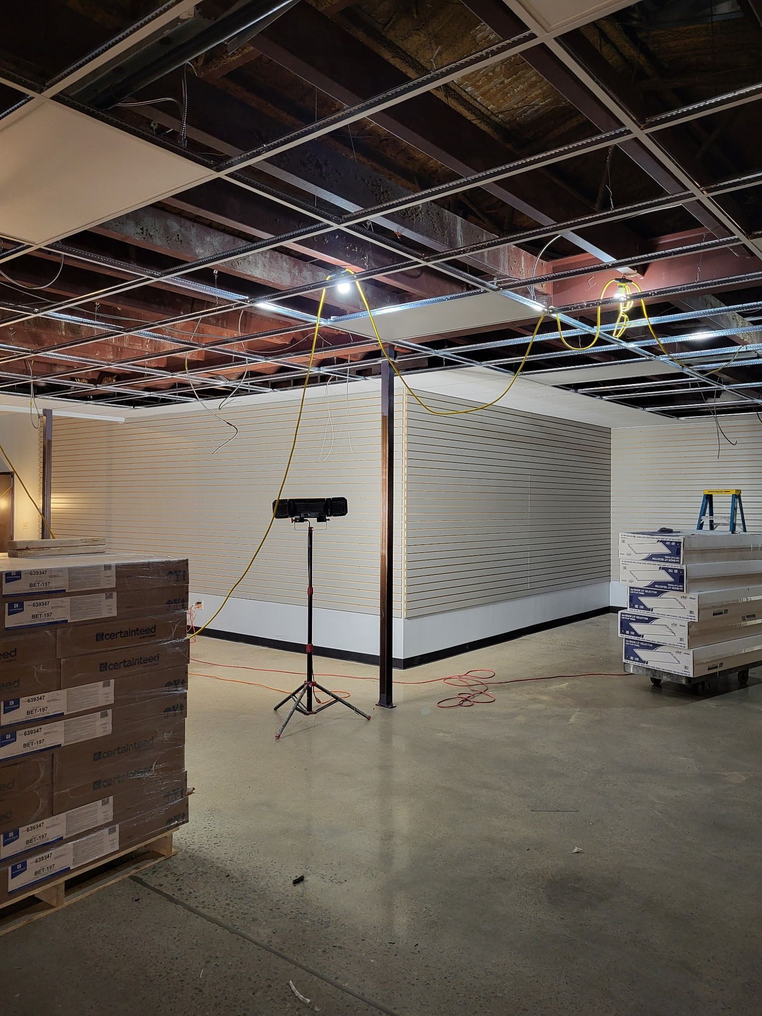 Interior construction site with finished white paneled walls, exposed ceiling, and equipment.