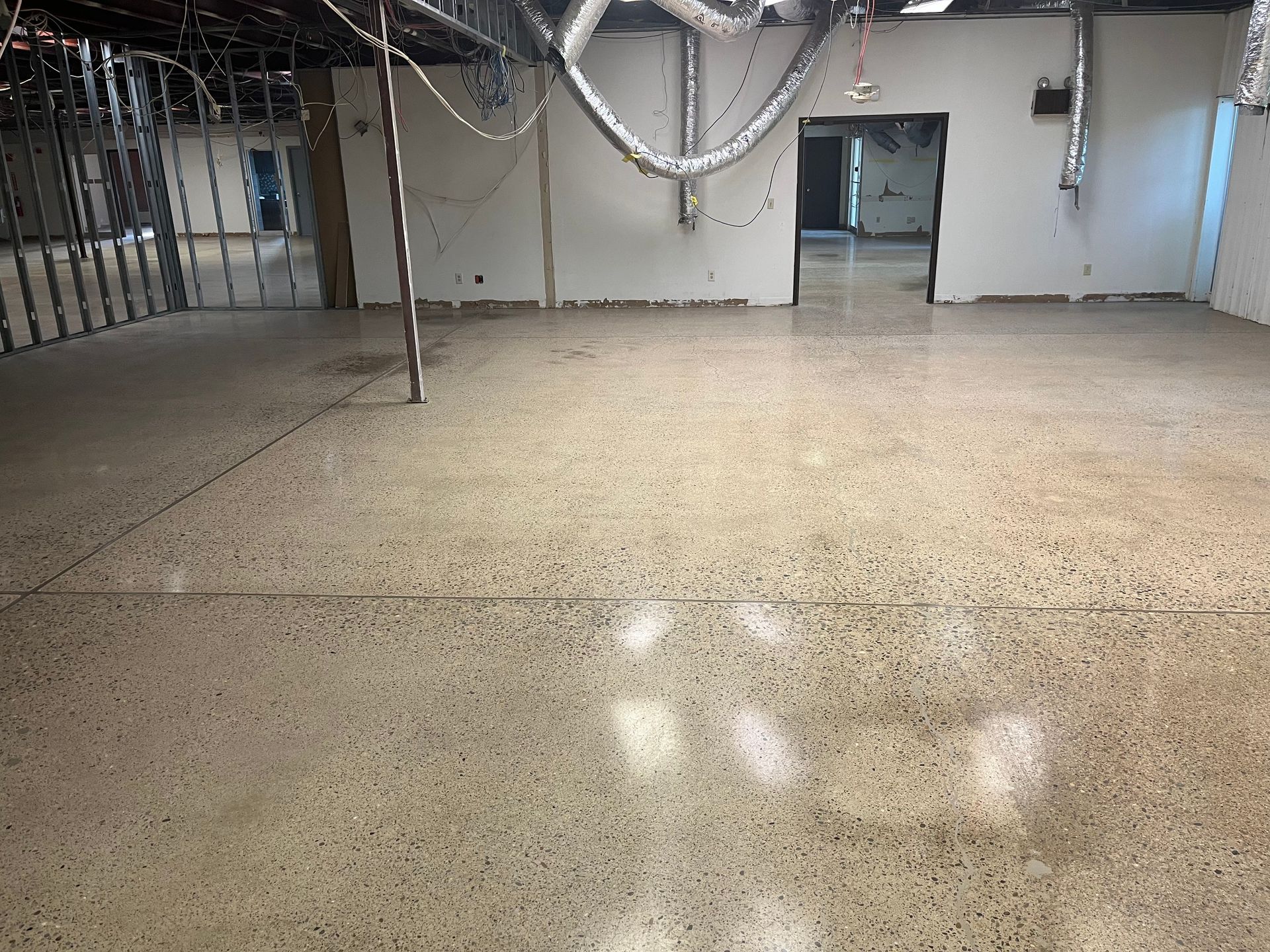 Bare concrete floor in a partially constructed room with exposed pipes and unfinished walls.