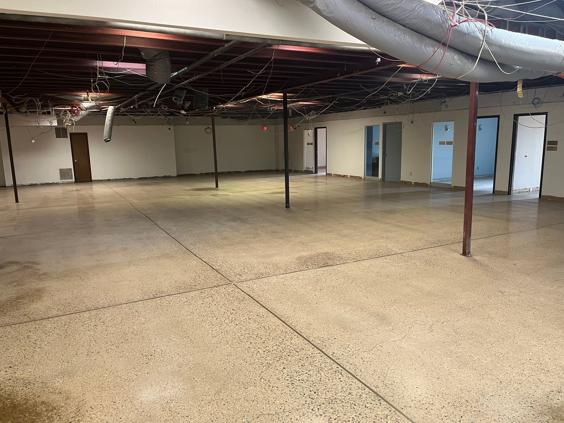 Empty commercial space with concrete floor, exposed ceiling, support poles, and doorways.