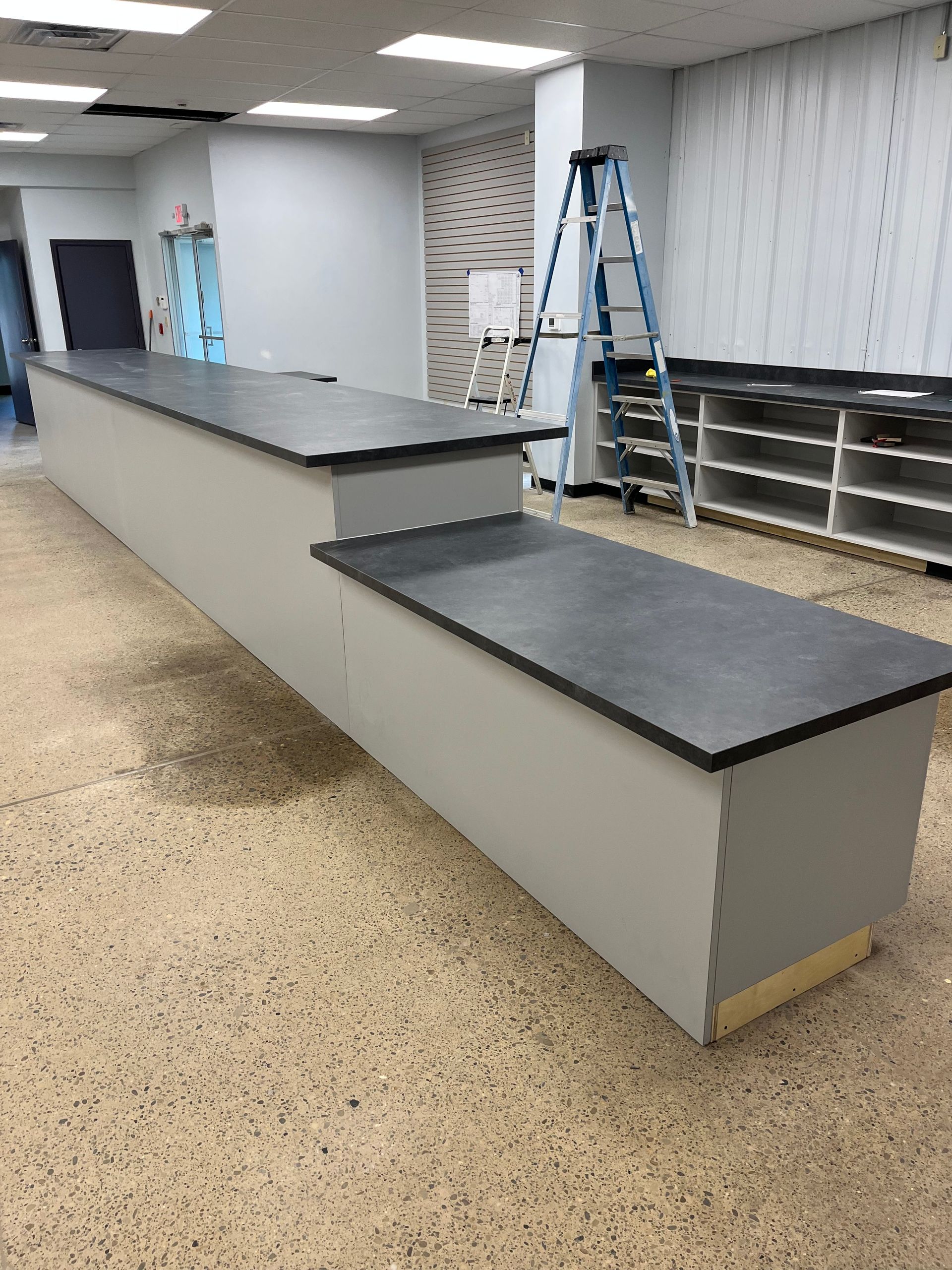Gray counter with black surface in a room, with a ladder and shelving in the background.