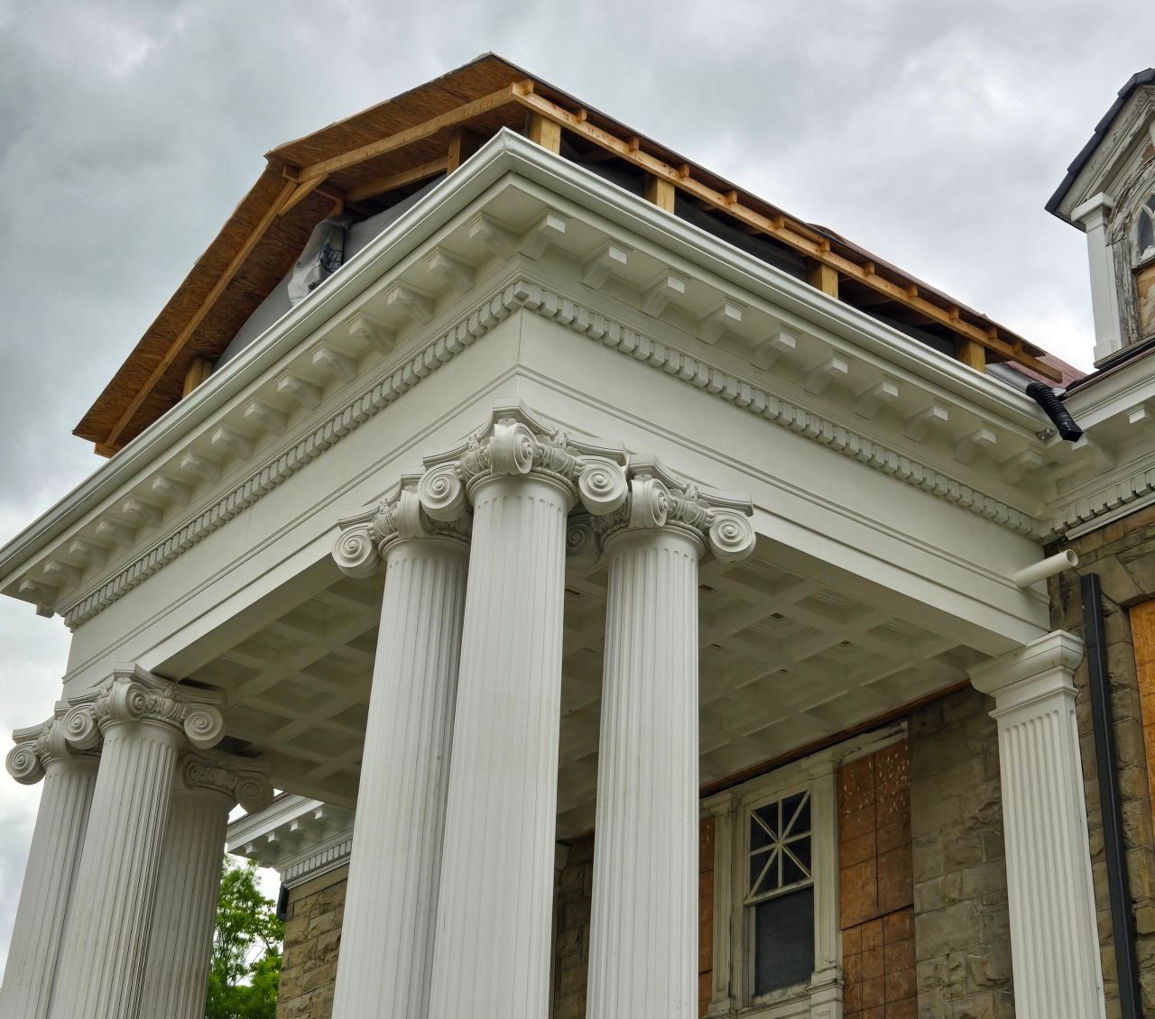 White-columned building with wooden roof under construction. Gray sky in the background.