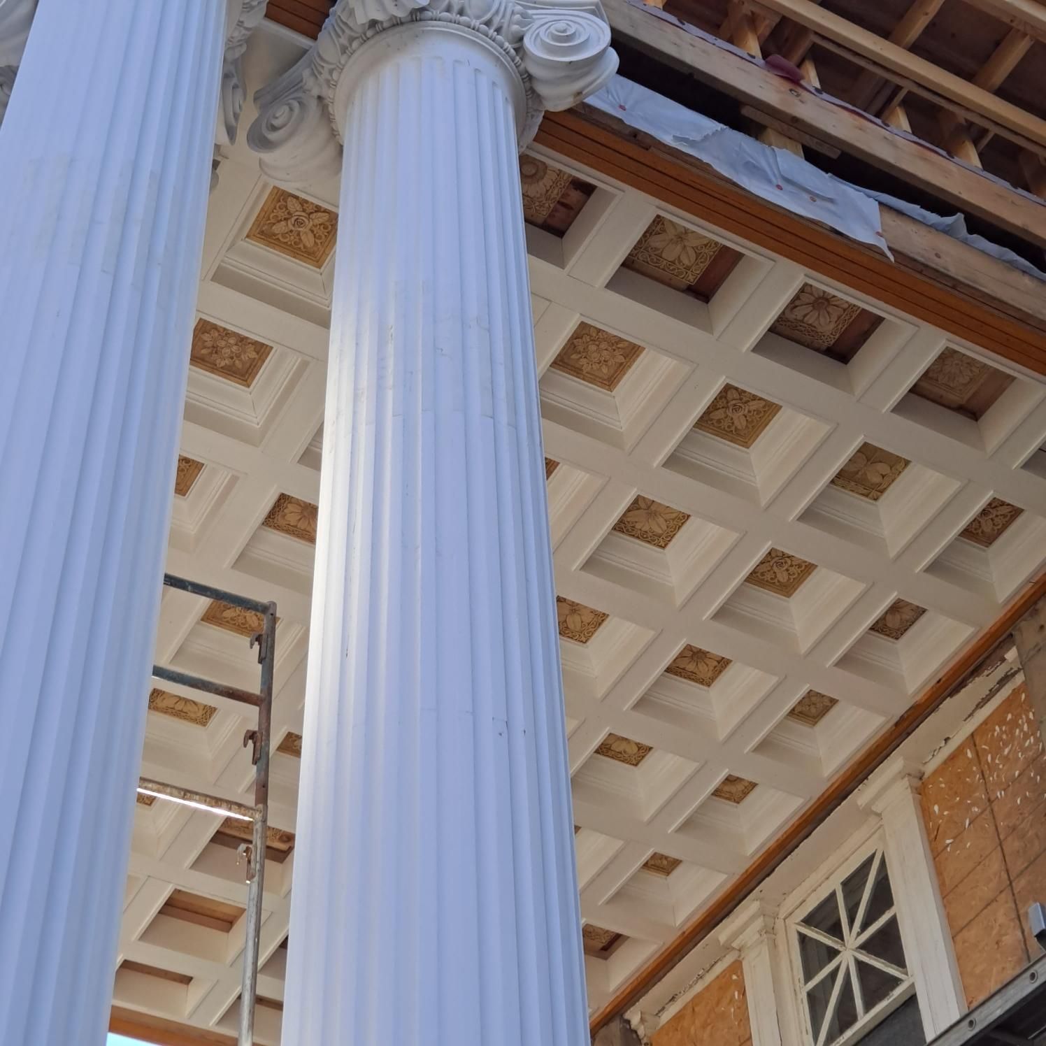 White columns supporting a coffered ceiling with gold detailing, exterior view.