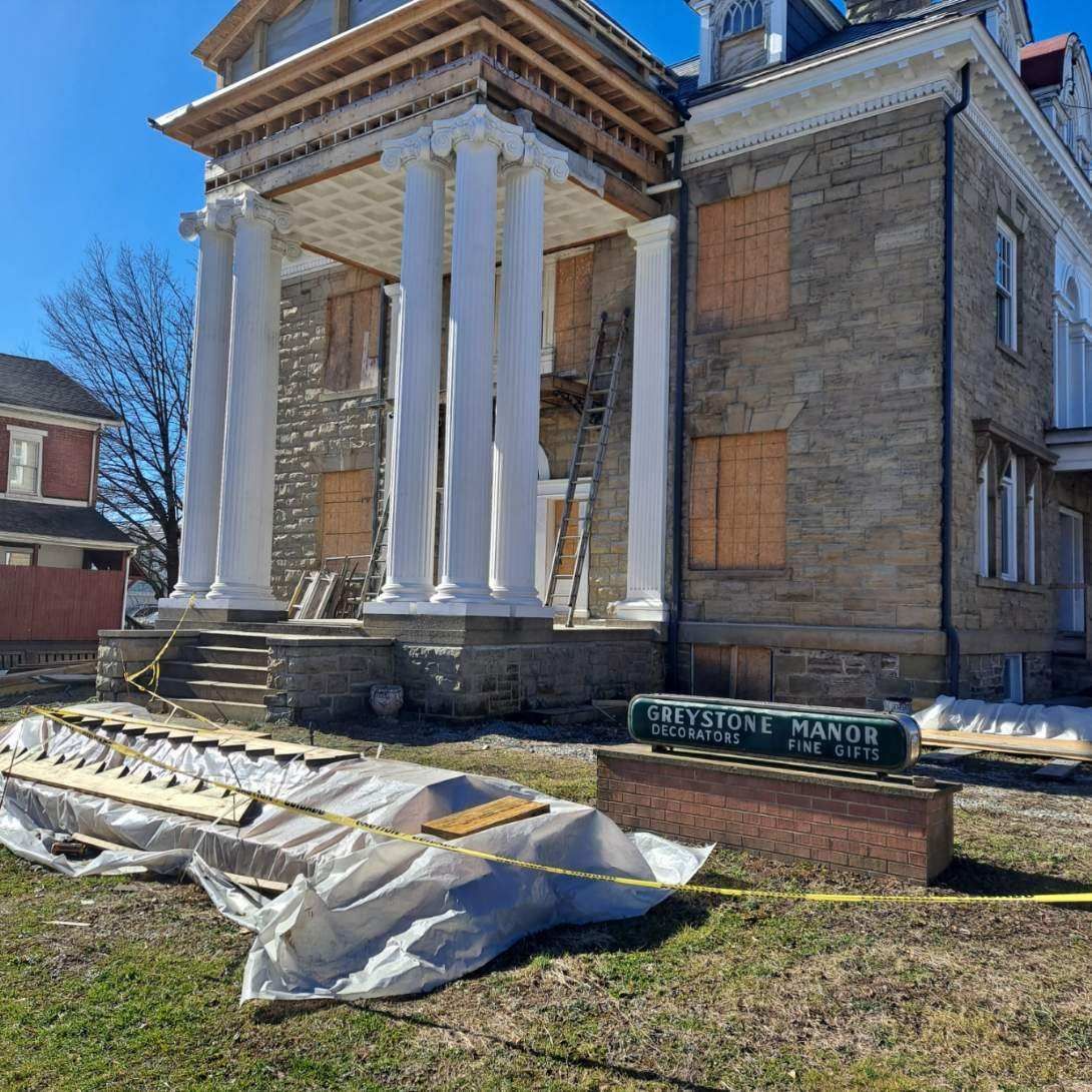 Stone mansion under construction; columns and boarded windows visible. 