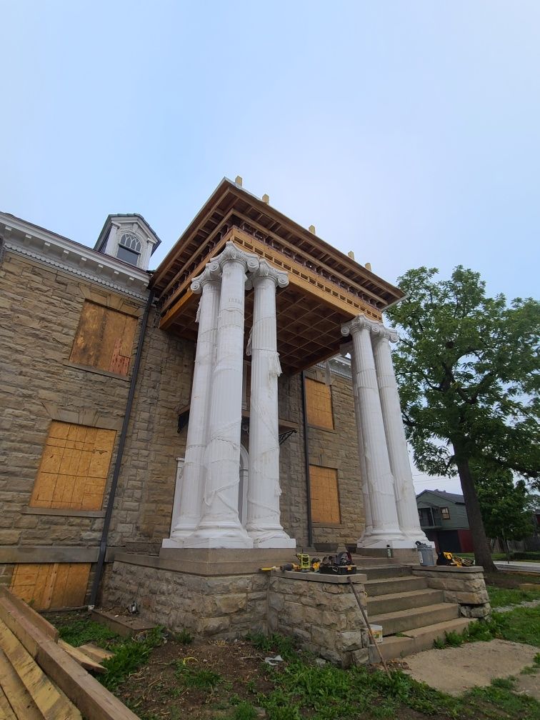 Stone building with a portico supported by white columns under construction. Wooden planks visible.