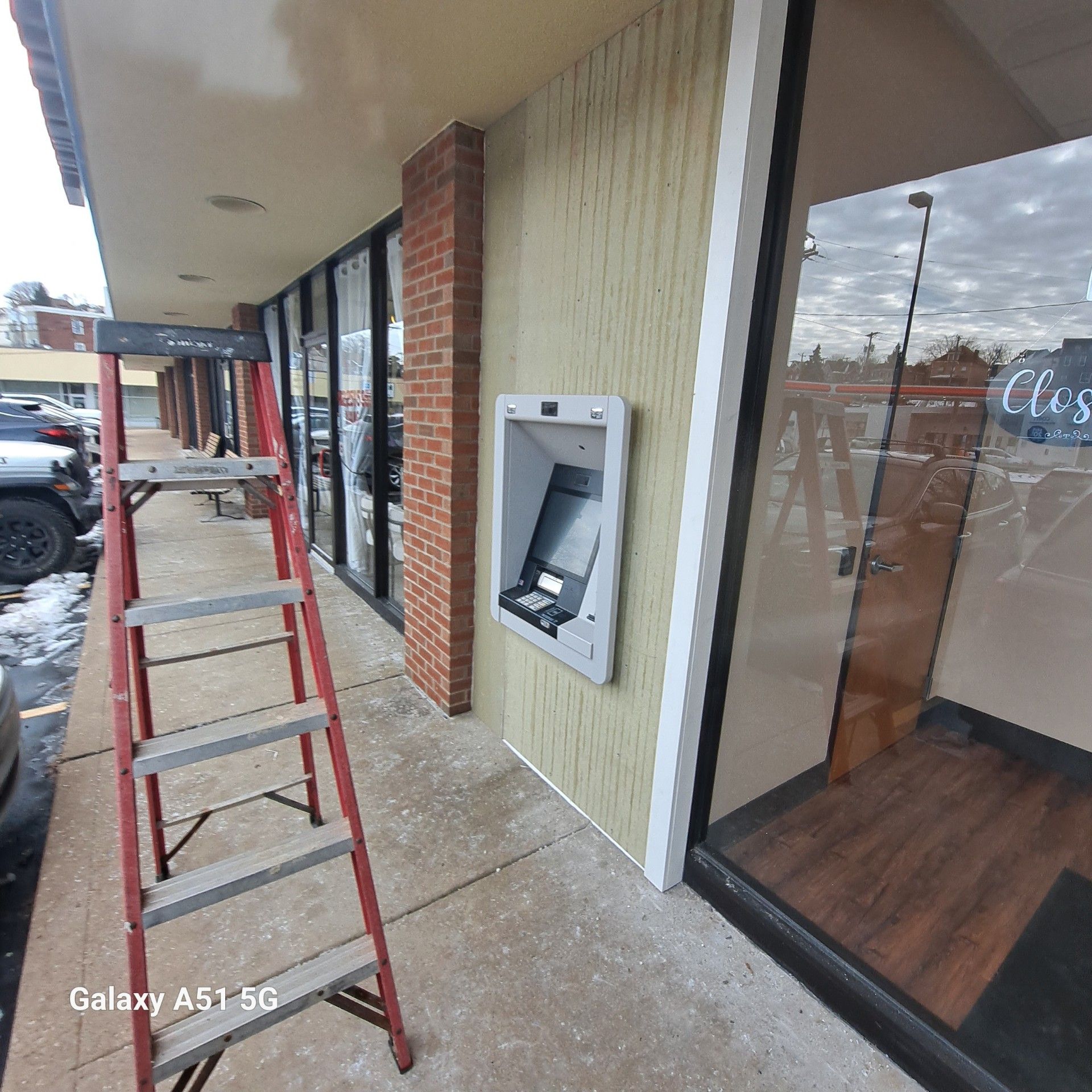 Red ladder next to a building's exterior with an ATM and windows.