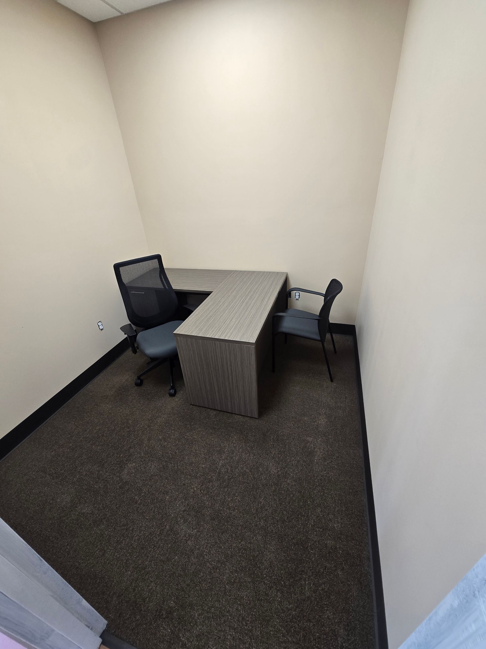 Small office with desk and chairs; carpeted floor and beige walls.