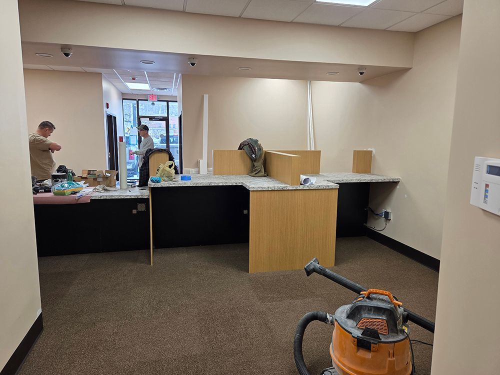 Interior view of a business under renovation; desks and vacuum cleaner are visible. Two people in the background.