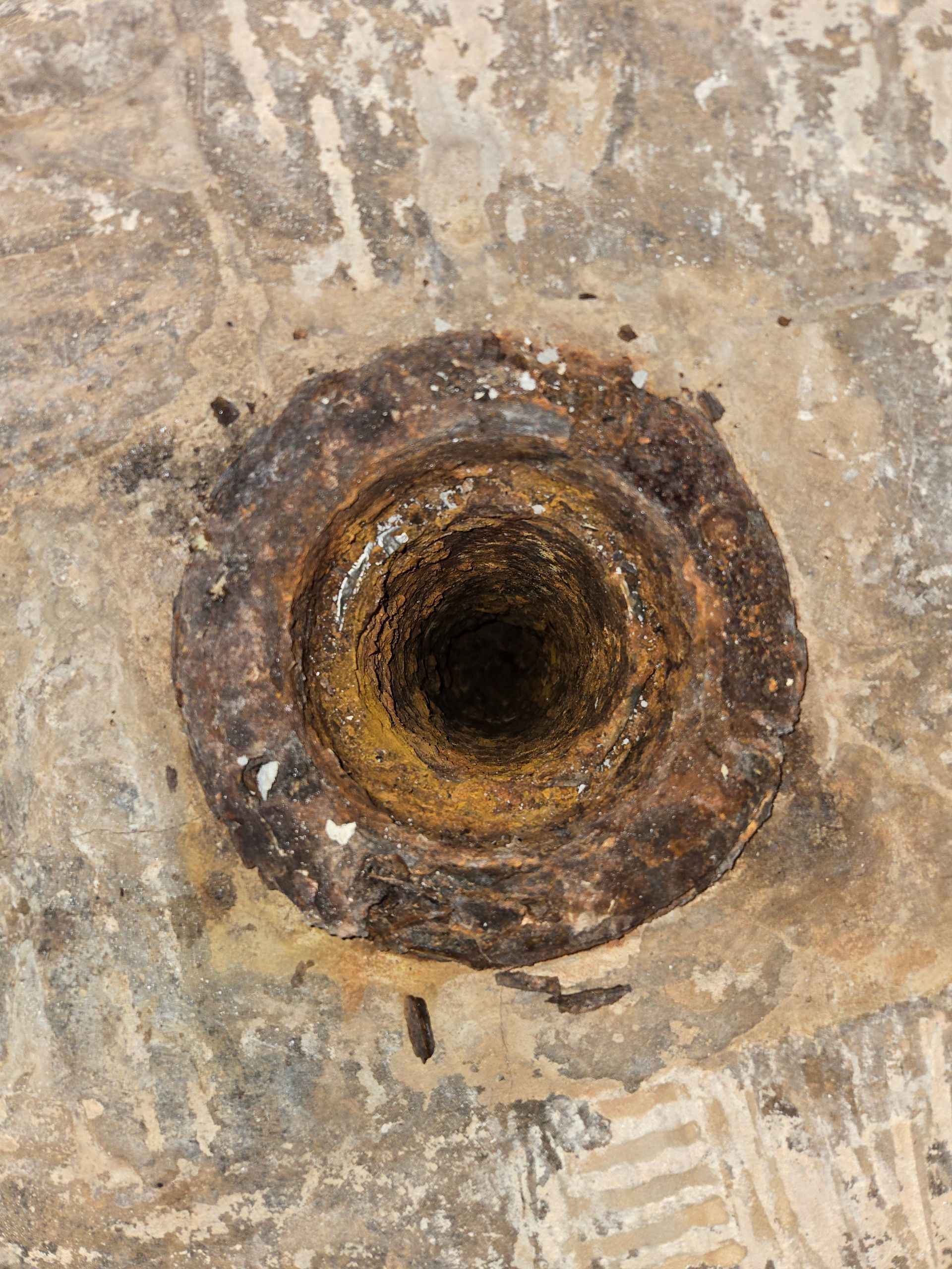 Rusty, circular drain in concrete. Dark opening, yellow and brown corrosion.