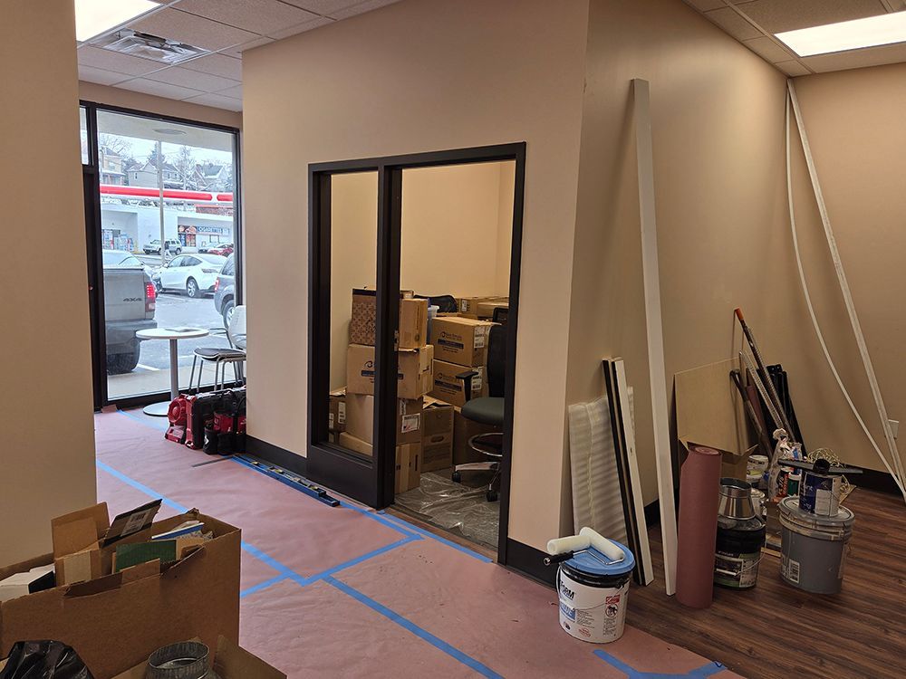 Interior view of an office space under renovation. Boxes and supplies clutter the area with two glass-paned doors.