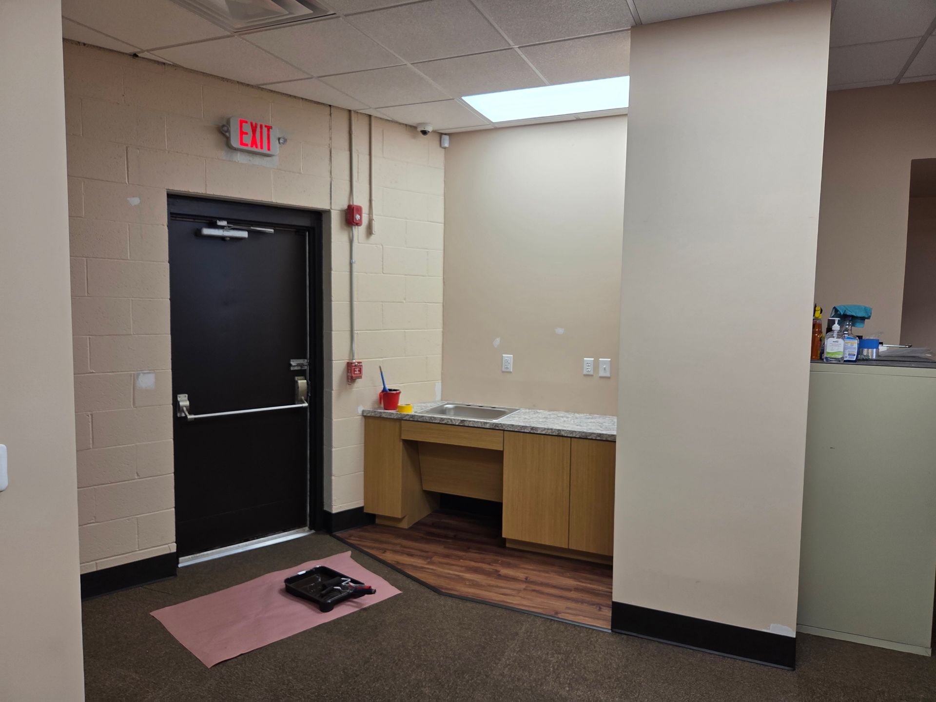 Interior office space with black door, beige walls, small desk, and exit sign.