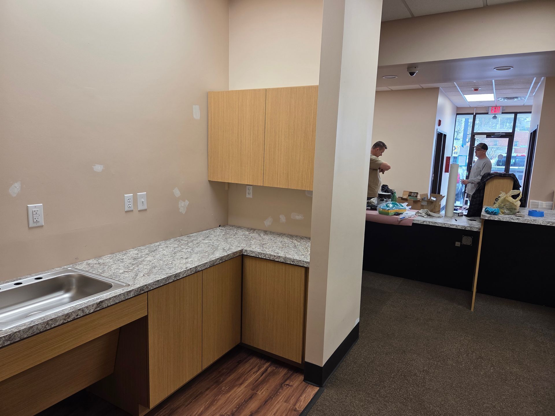 Interior with sink, cabinets, countertop, two people in background near an entrance.