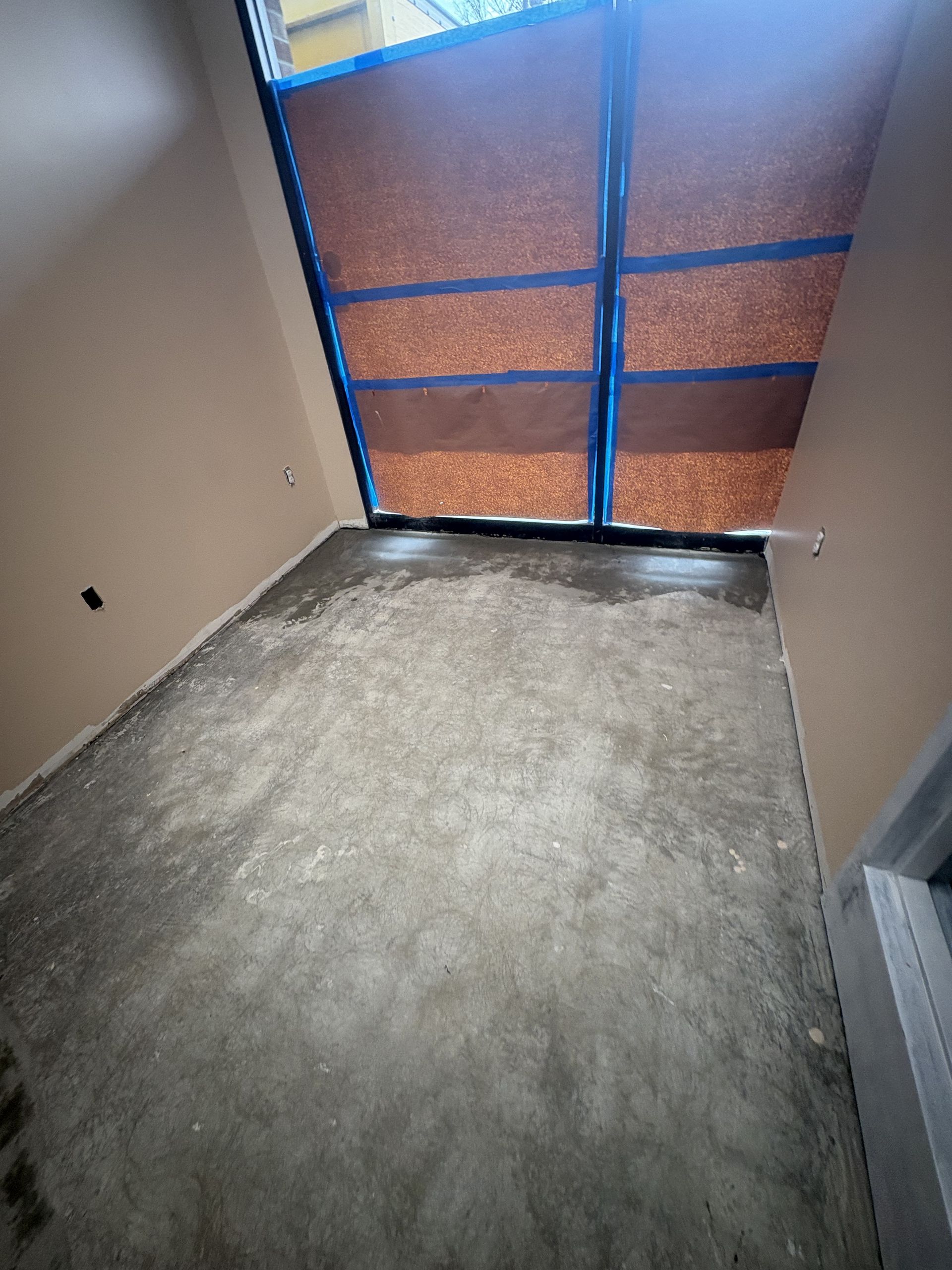 Room with concrete floor and closed door/window with brown panels and blue tape.