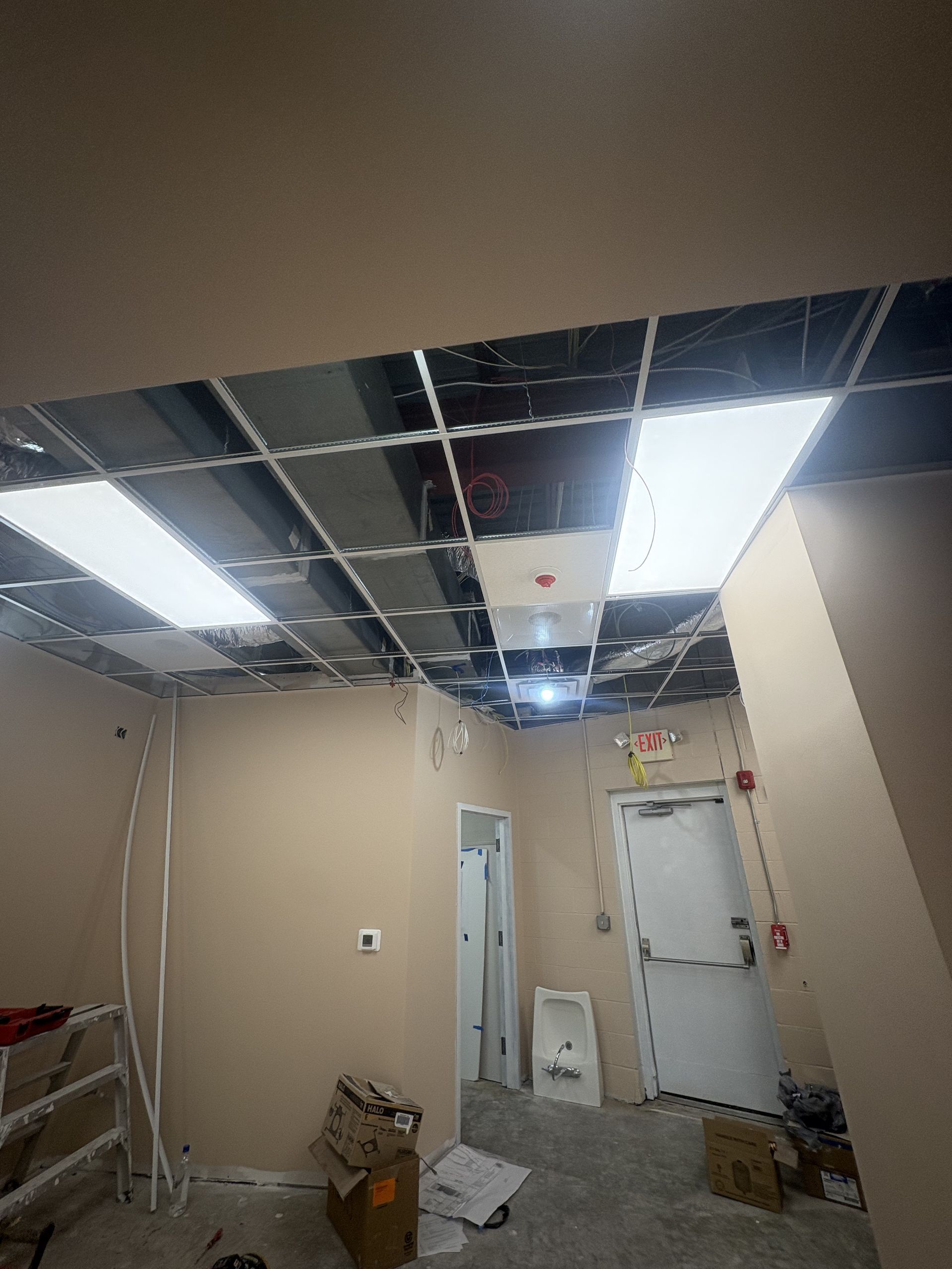 Interior ceiling under construction, with exposed metal grid, recessed lighting, and beige walls.
