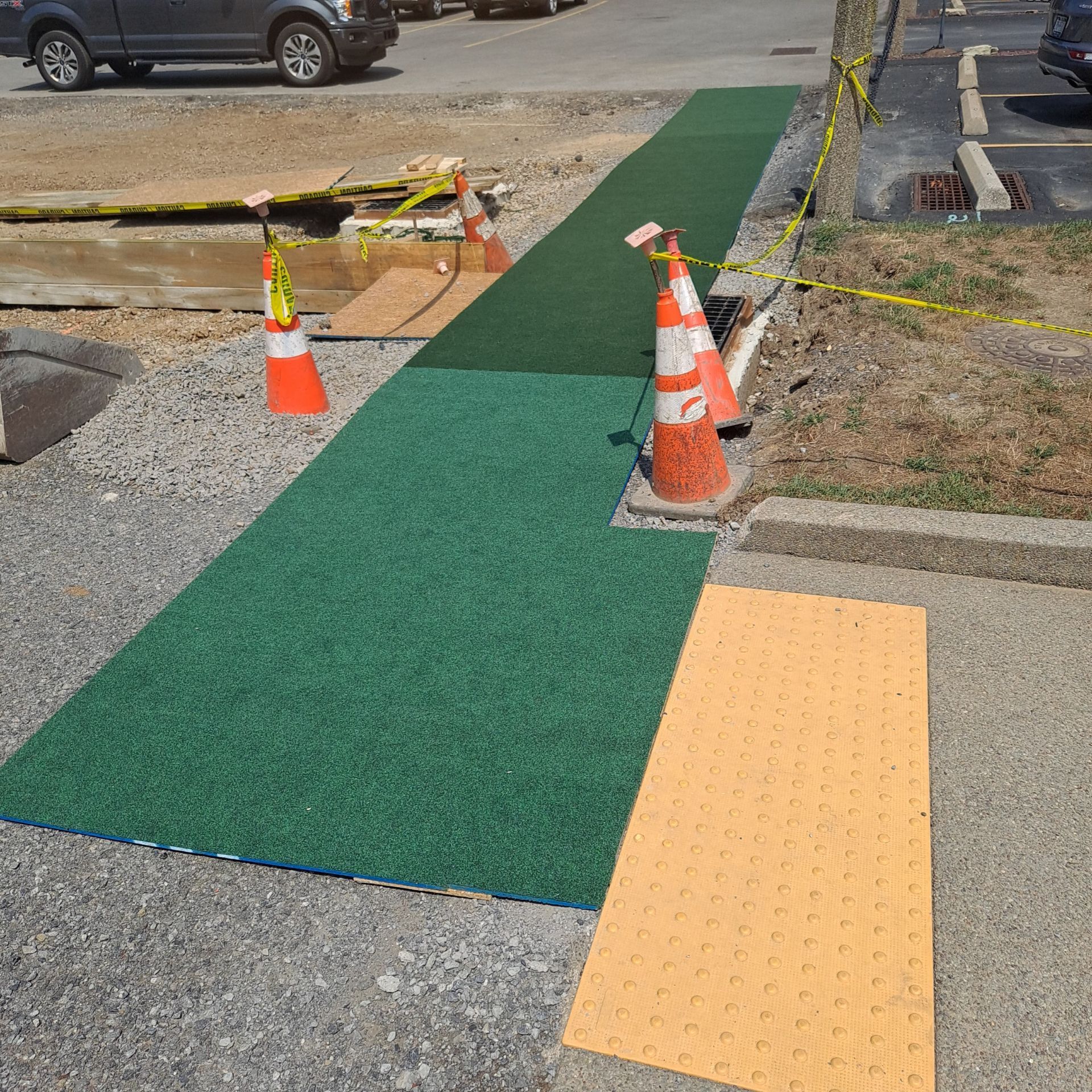 Green and yellow temporary walkway with cones, next to a construction site, on a sunny day.