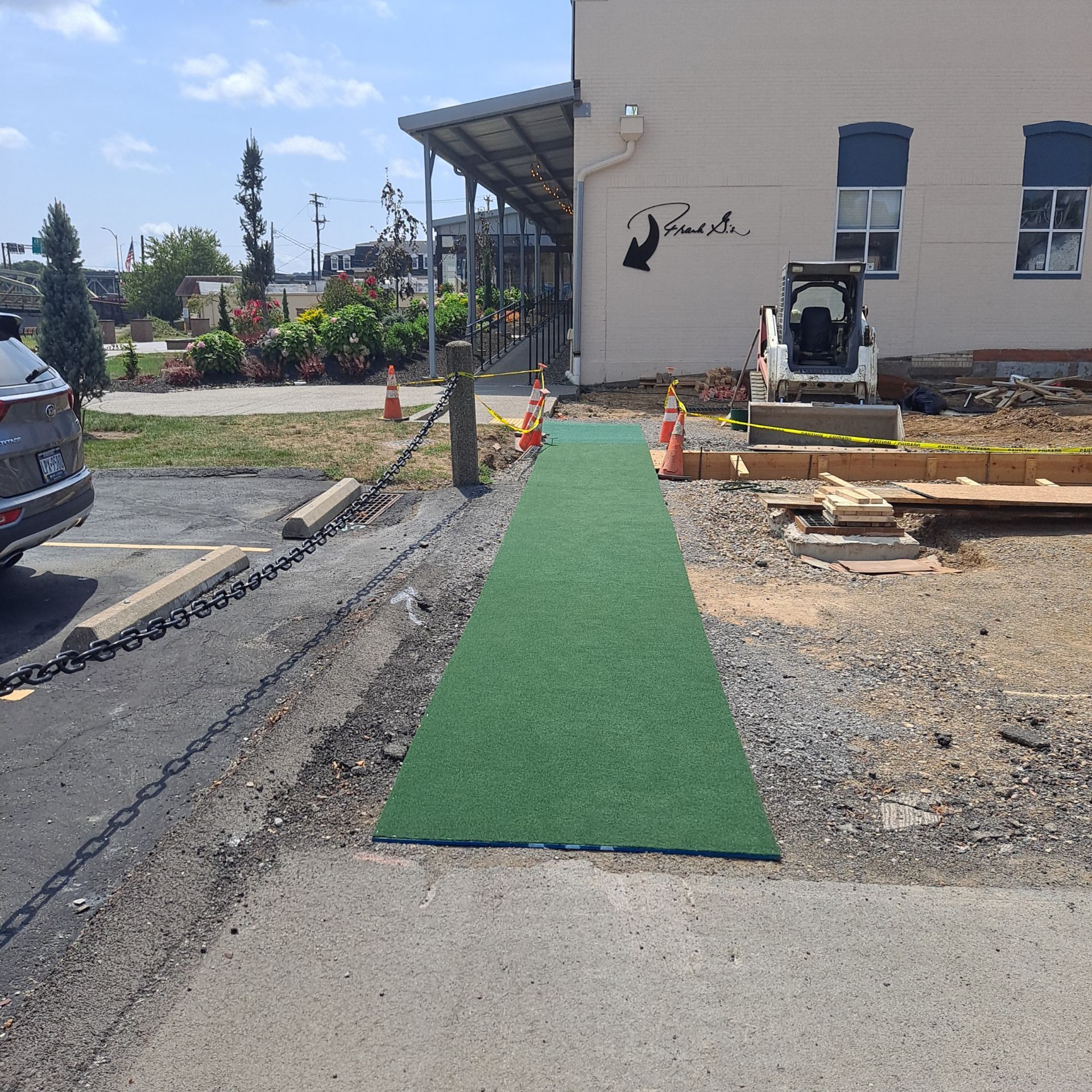 Green pathway leading to a building with construction on the right. A car is on the left.