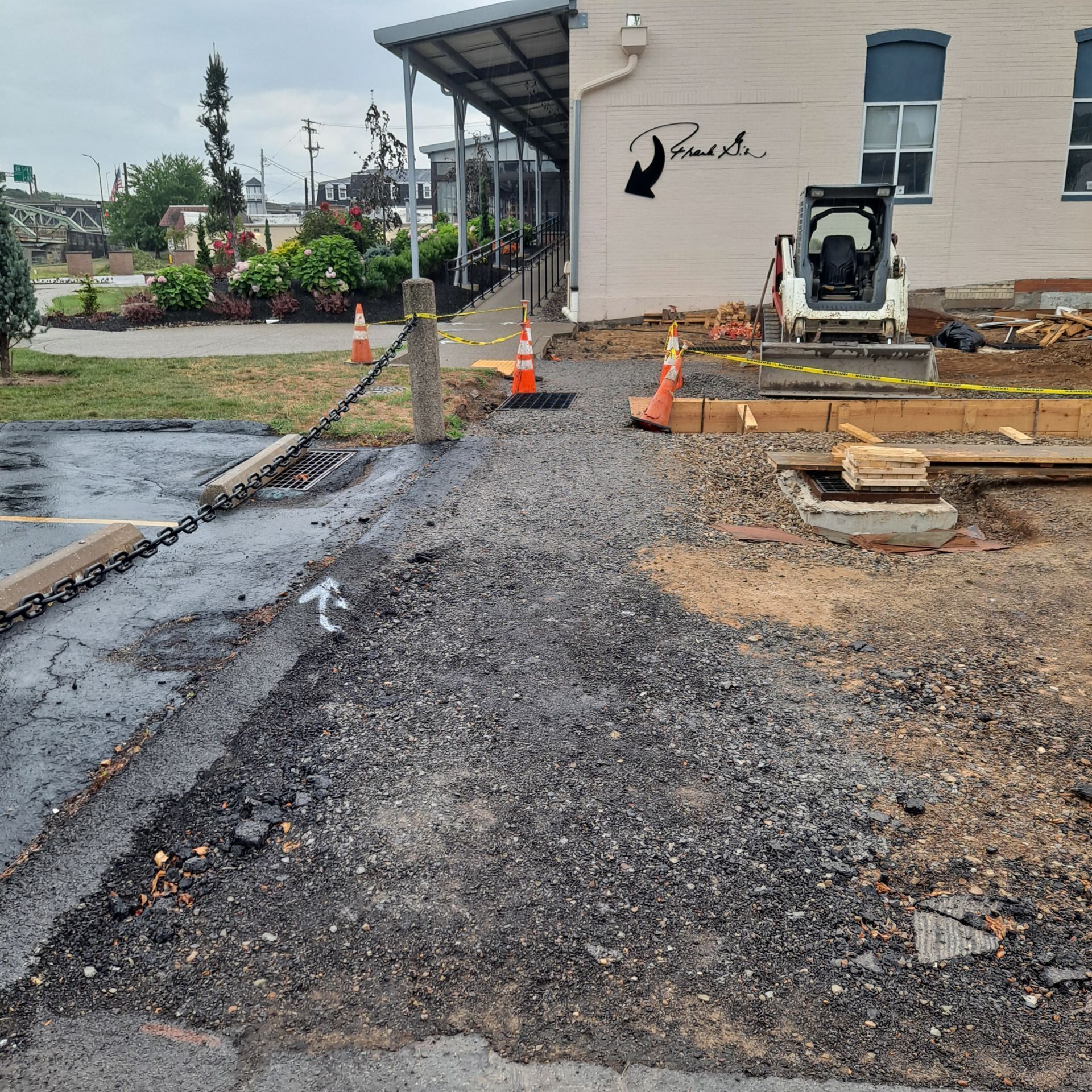 Construction site. Asphalt and gravel path with barriers and small construction equipment next to a building.