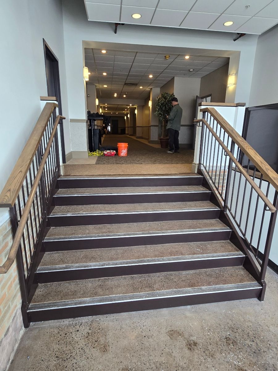 Stairs leading into a hallway; brown handrails, textured steps. A person stands inside the hallway.