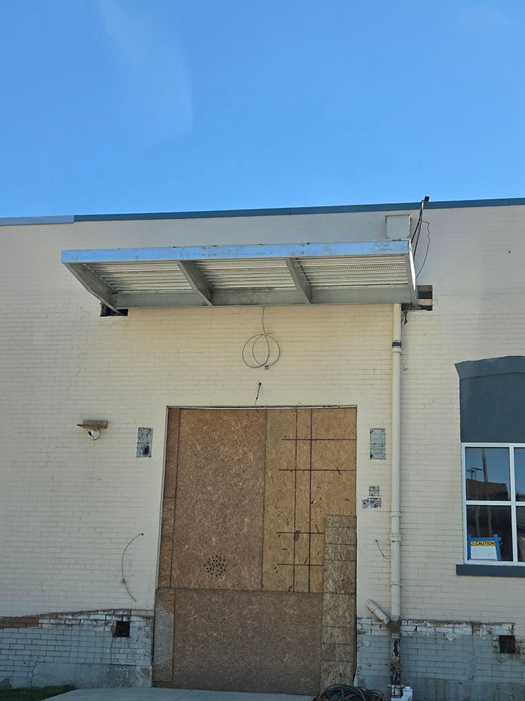 Boarded-up doorway under a metal awning on a beige brick building; light blue sky.