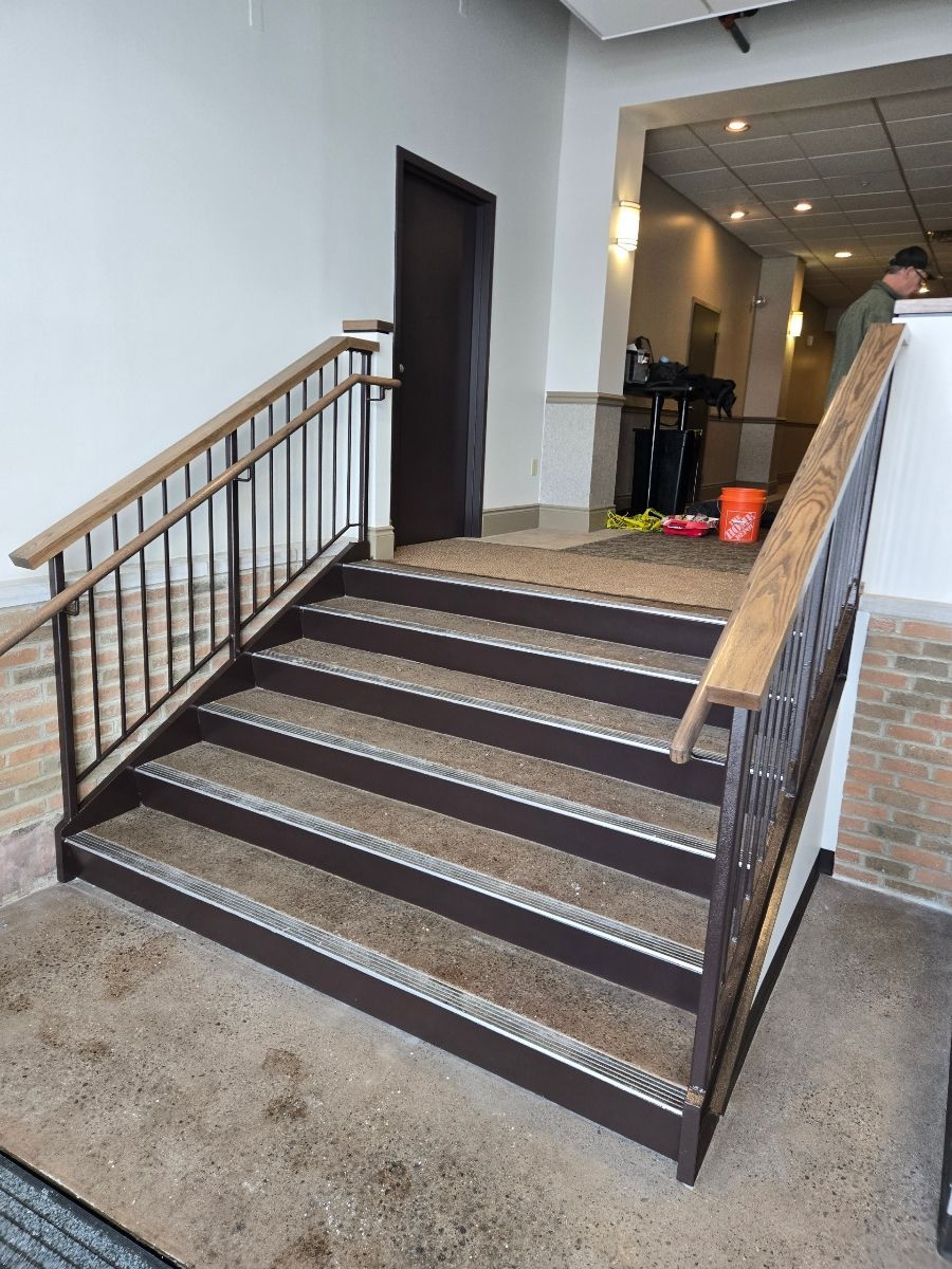 Metal stairs with brown treads and handrails, leading to a brown door inside a building.