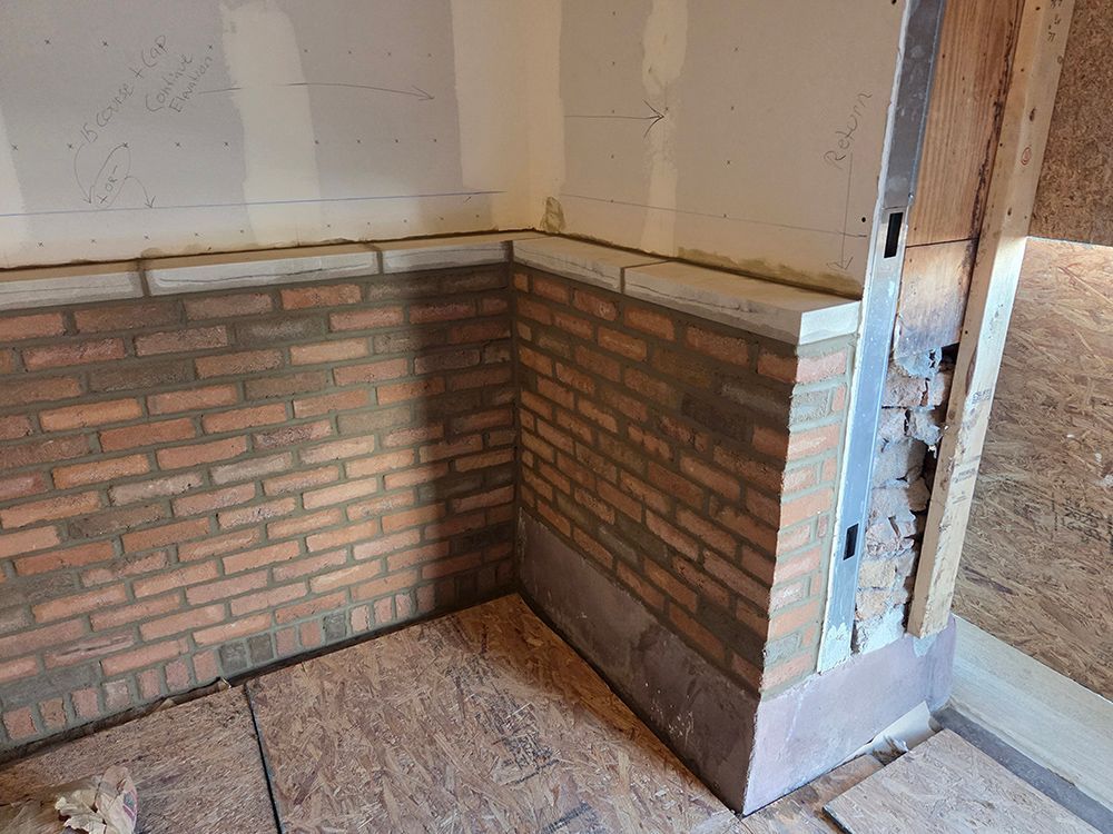 Corner of a room under construction with red brickwork, wooden framing, and light-colored walls.
