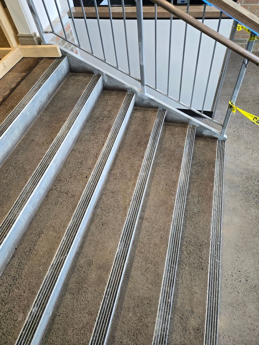Concrete stairs with metal handrail and textured safety strips. Yellow caution tape on the right.
