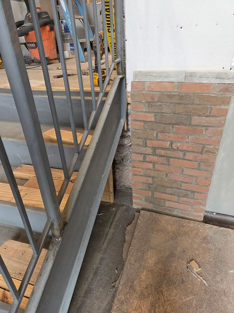 Staircase with metal handrail. Brick wall adjacent. Ground level concrete, stairs wooden.