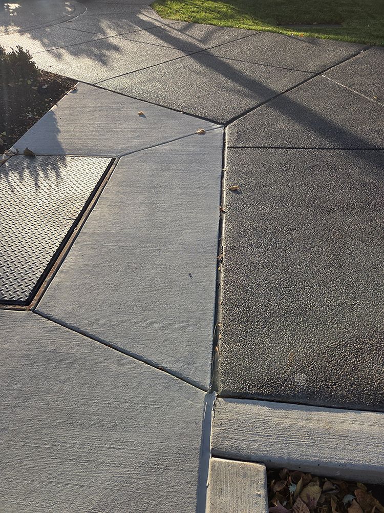 Concrete sidewalk with geometric shapes, some darker, a grate, and sunlight.