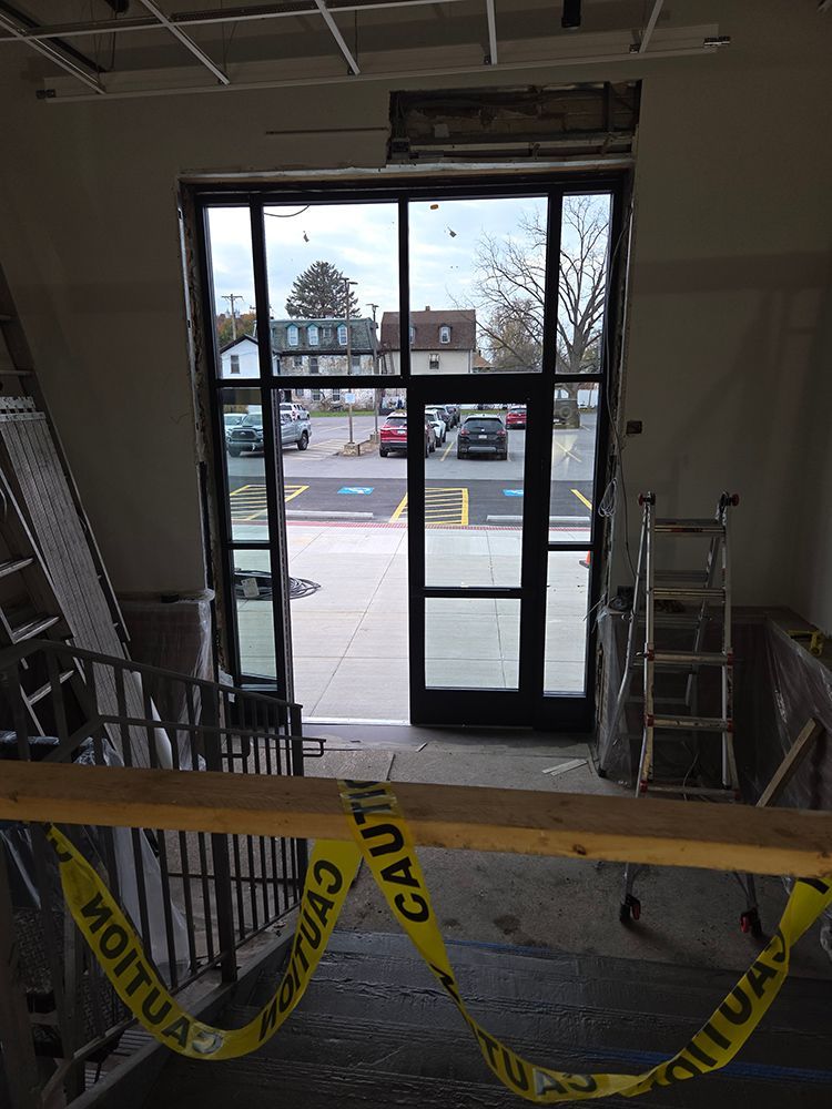 View from inside a building through a large glass door with caution tape, looking out at a parking lot.