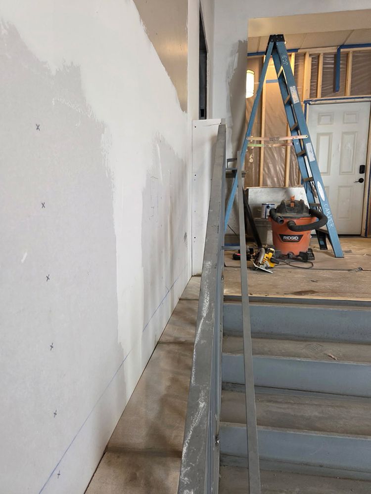 Interior staircase under construction with a handrail alongside a drywall-covered wall.