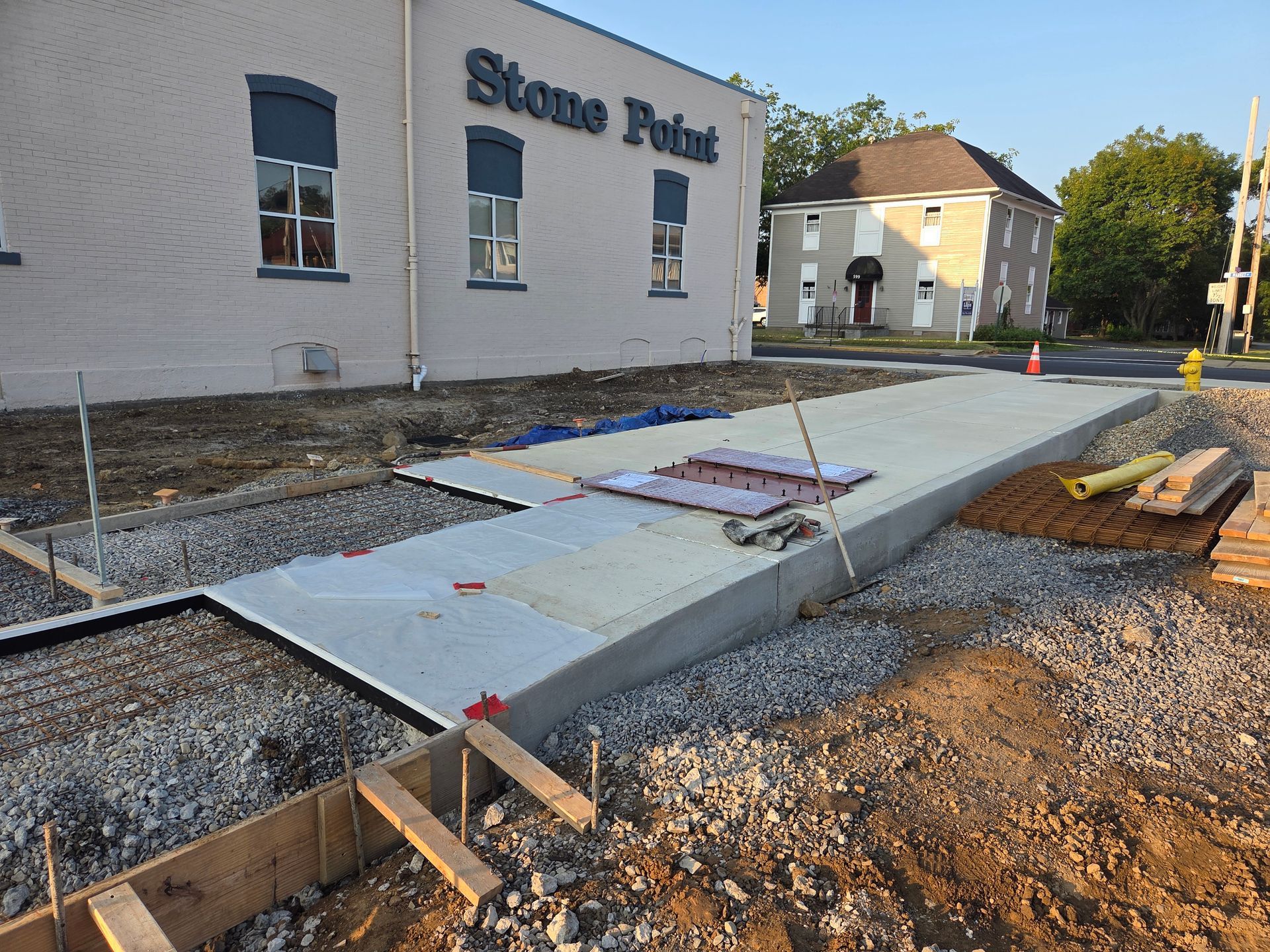Concrete construction site with building in background.  Gray and brown tones.  New sidewalk under construction.