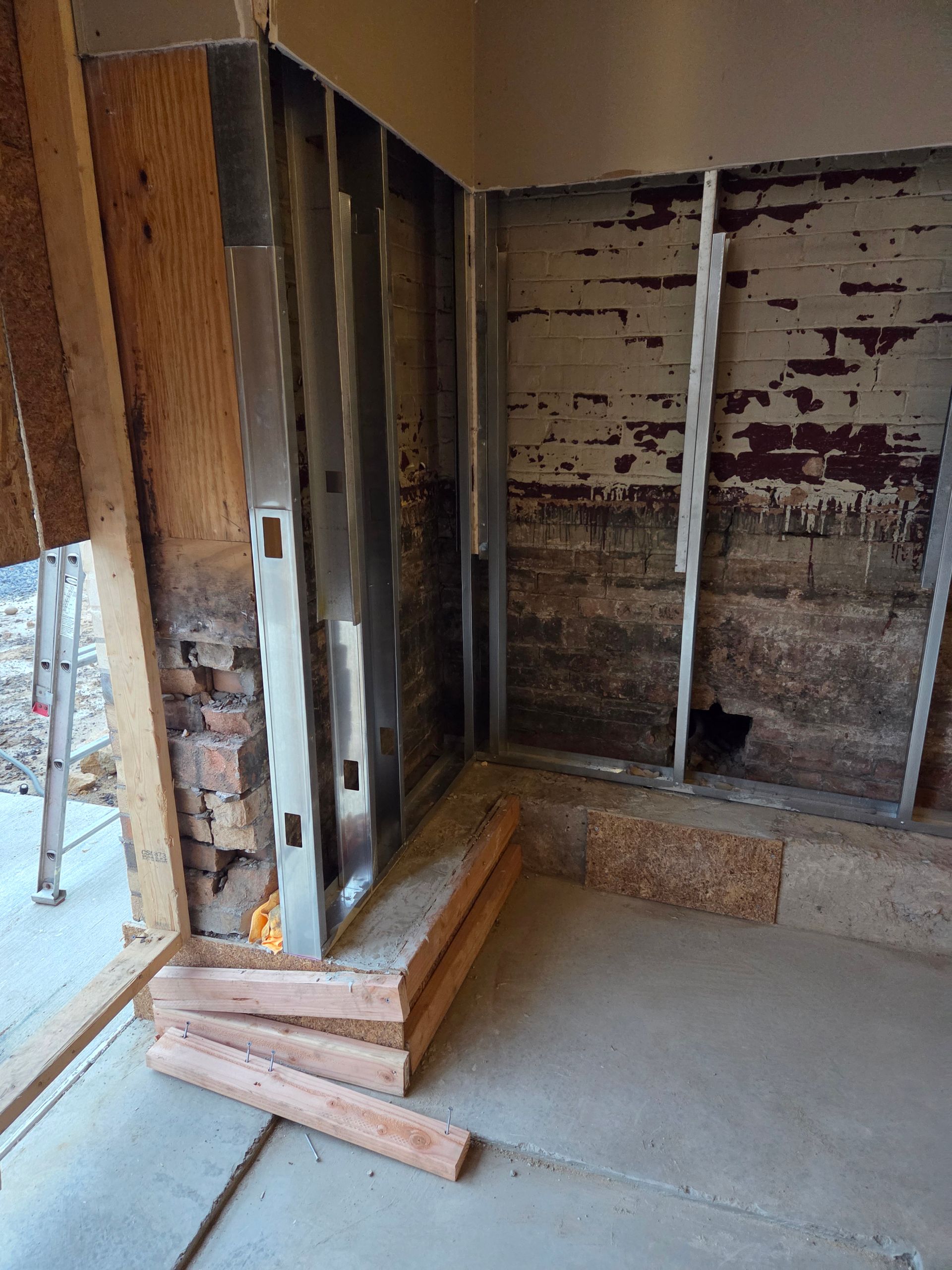 Interior room under construction, with exposed framing, concrete floor, and wooden beams.