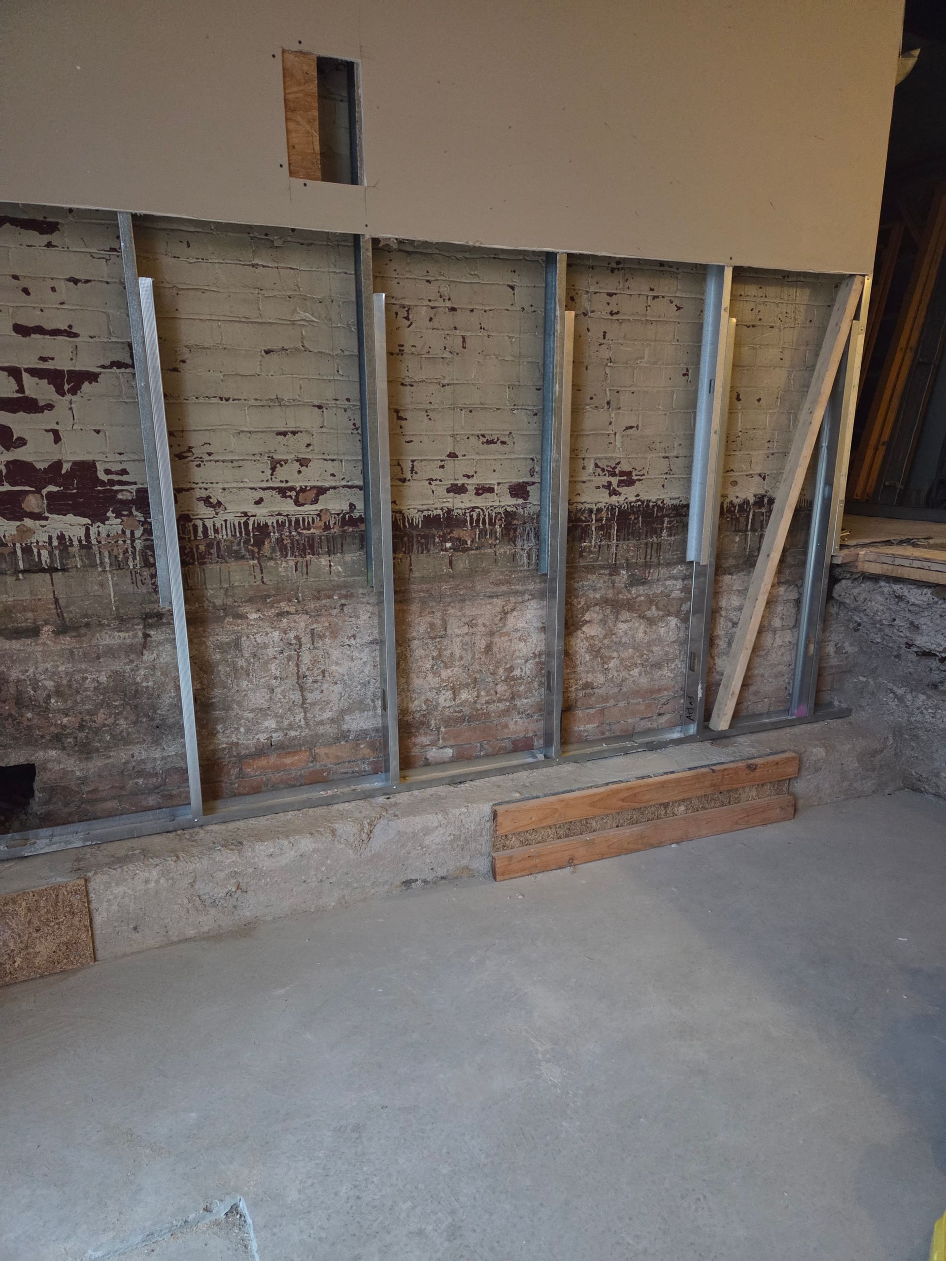 Interior of a building under construction. Brick wall with metal studs and wooden supports; concrete floor.