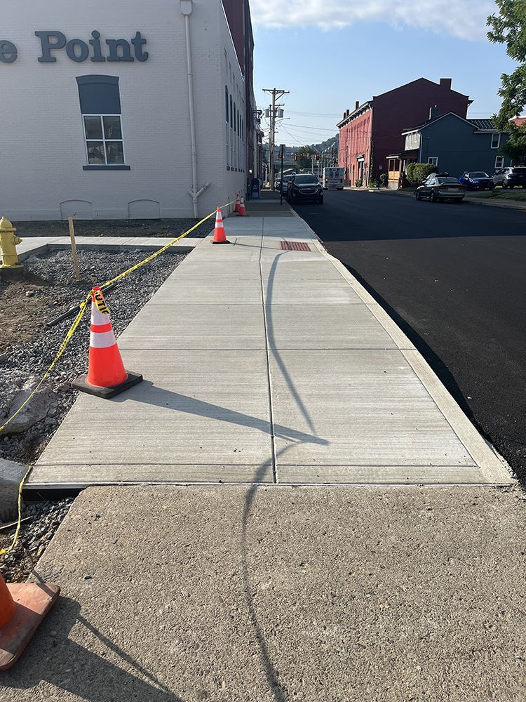 Newly constructed sidewalk next to a street, blocked by orange cones and caution tape.