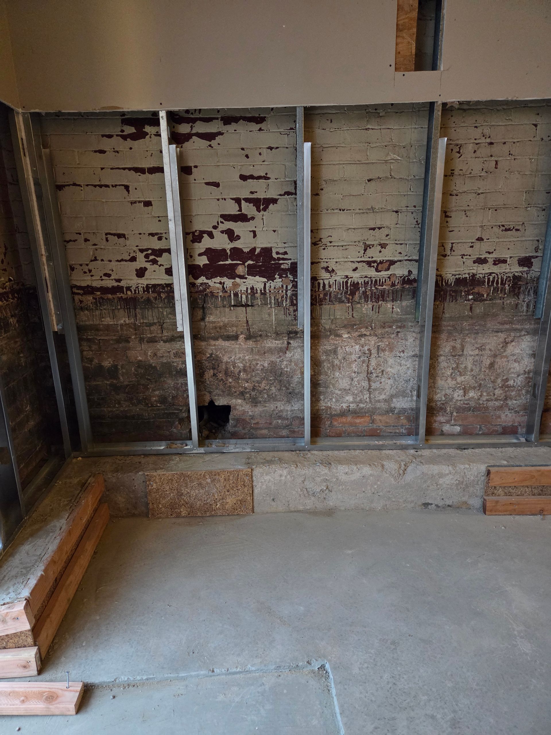 Interior of a room under construction with exposed wood, metal framing, and concrete floor.