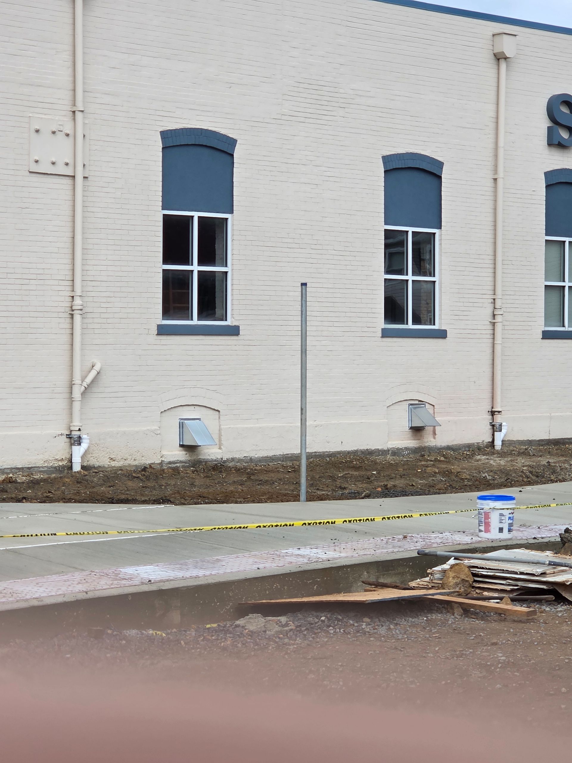 Beige building exterior with blue-topped windows, a pole, and caution tape along a muddy area.