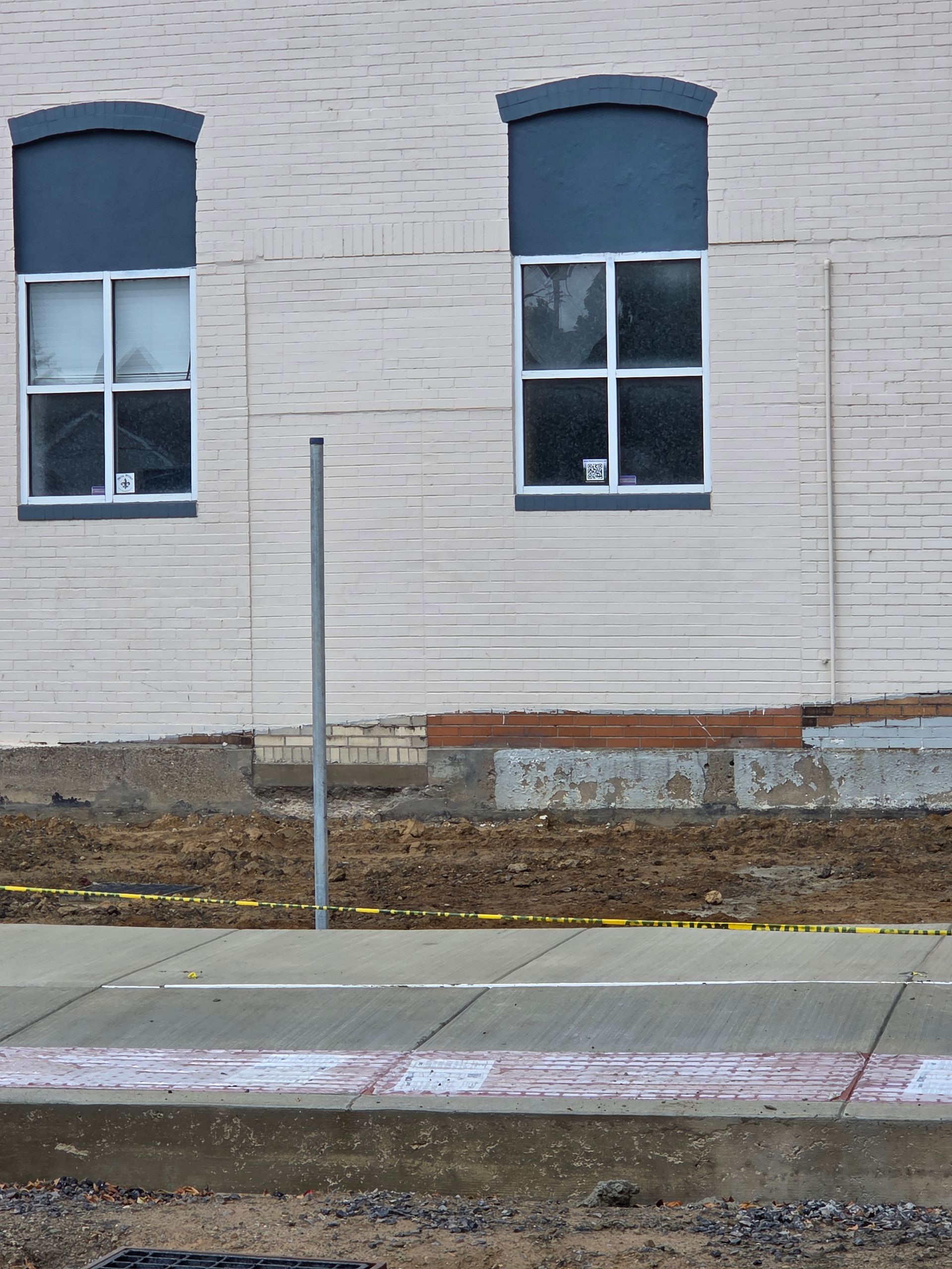 Two windows on a light brick building with blue trim. A sidewalk and construction area are in the foreground.