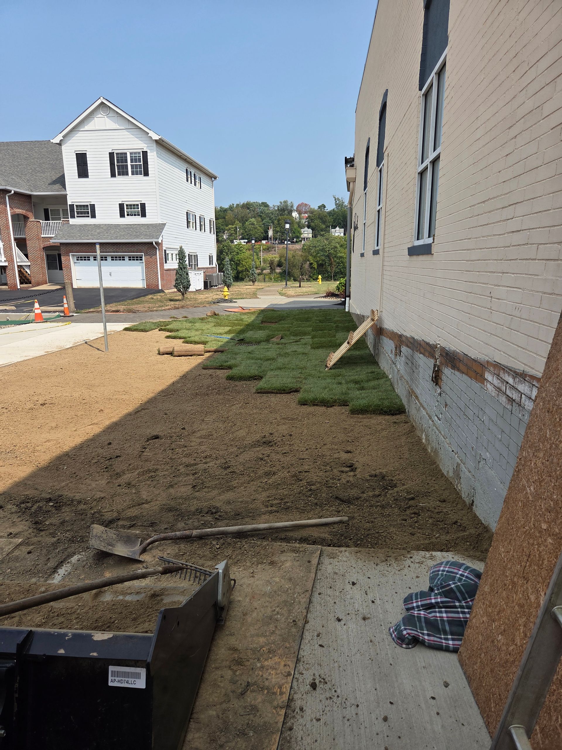Construction site with laid sod next to a building. Brown soil and buildings in the background on a sunny day.
