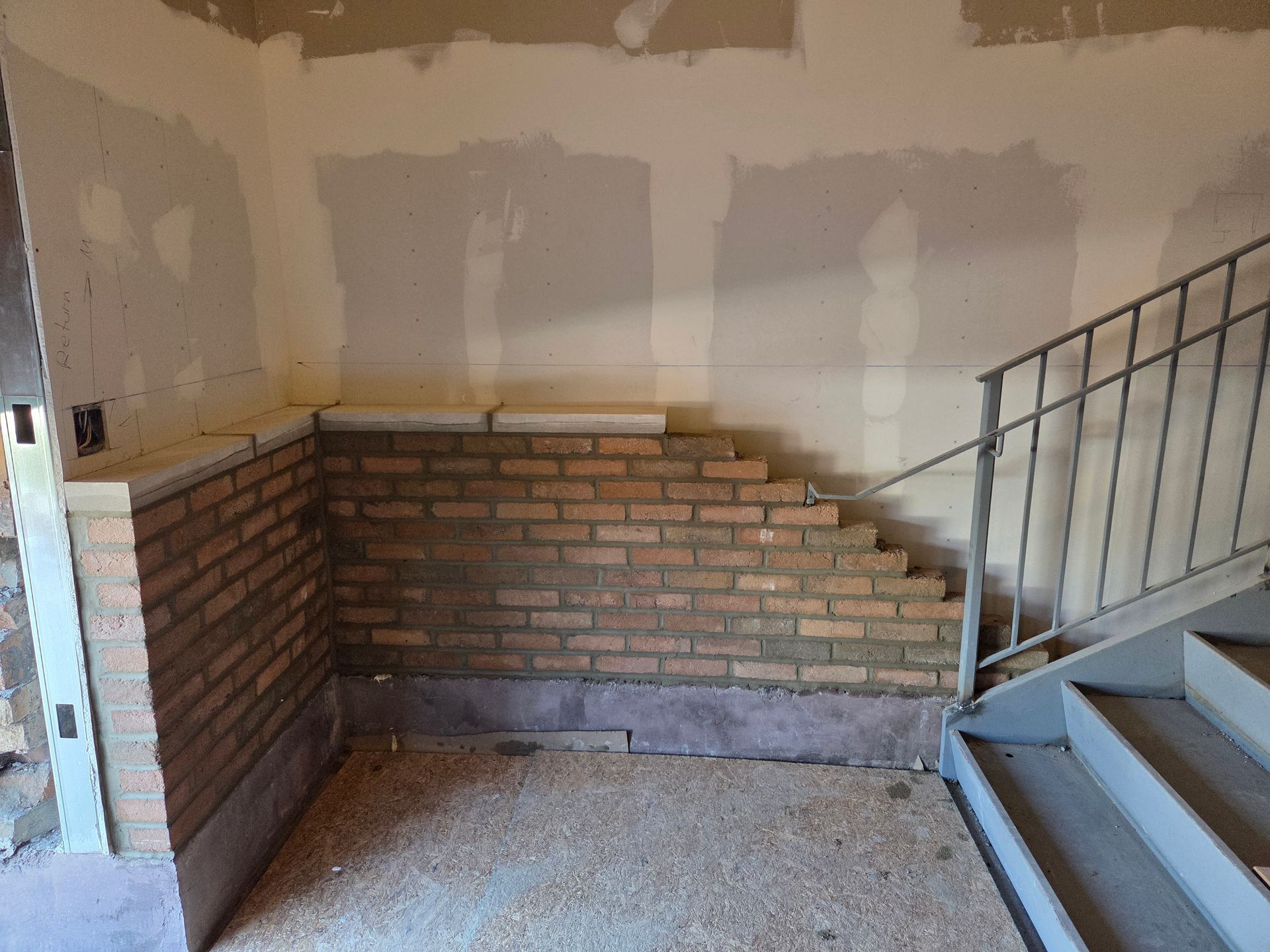 Interior with brick wall under construction next to a staircase.
