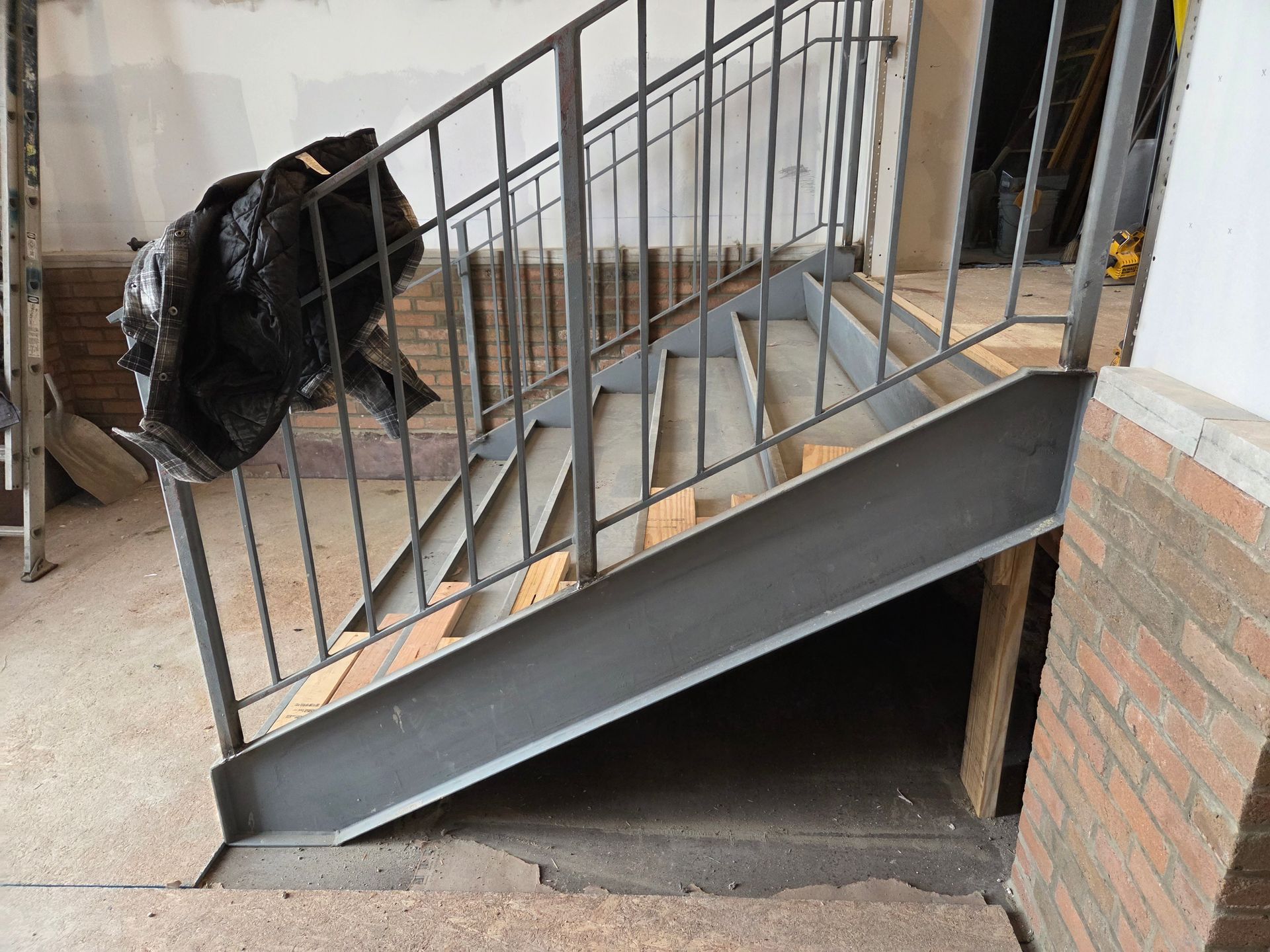 Steel staircase with metal railing in a construction setting; black garbage bag on the side.