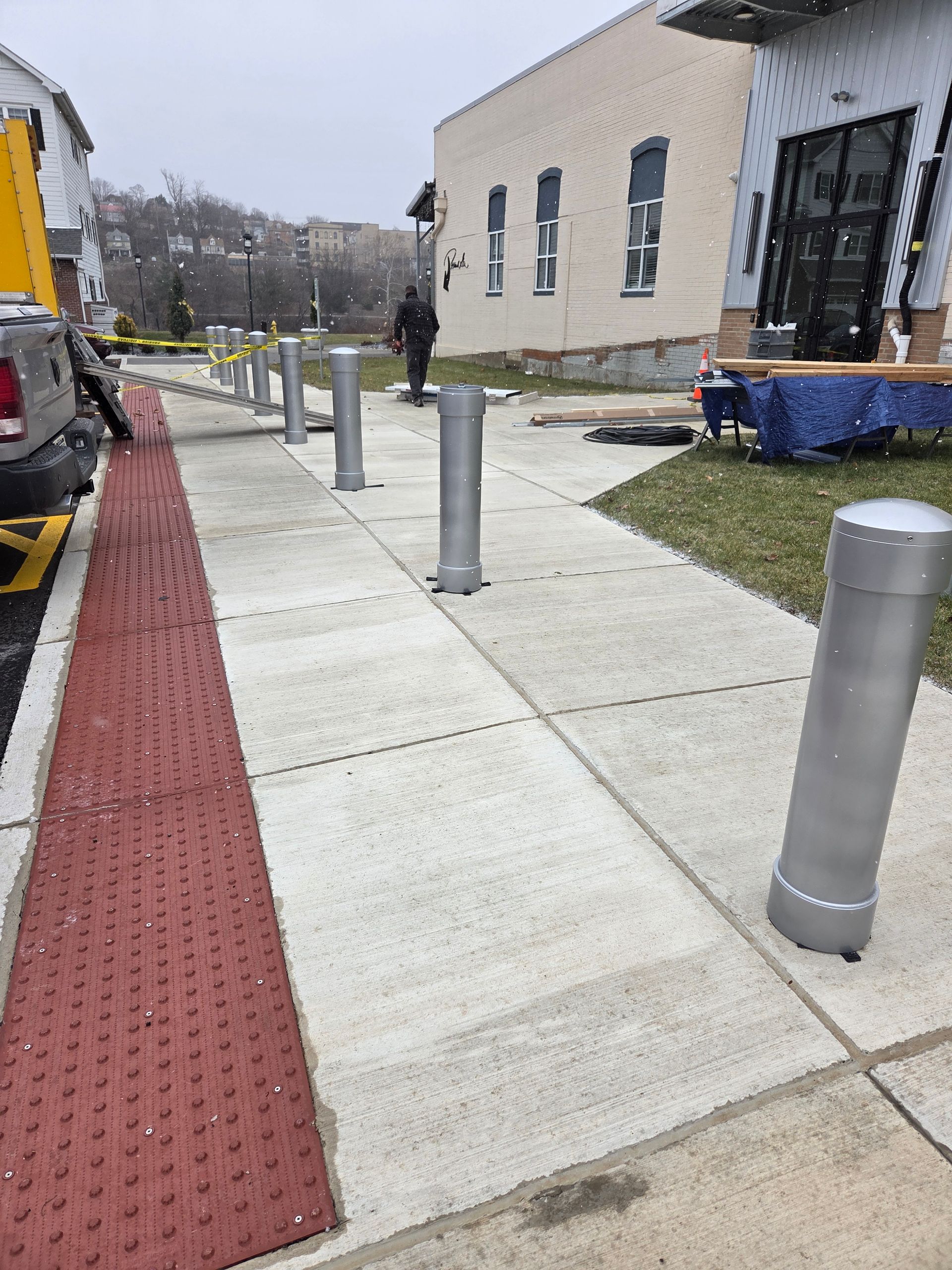 Sidewalk with metal bollards, tactile paving, and construction in progress.