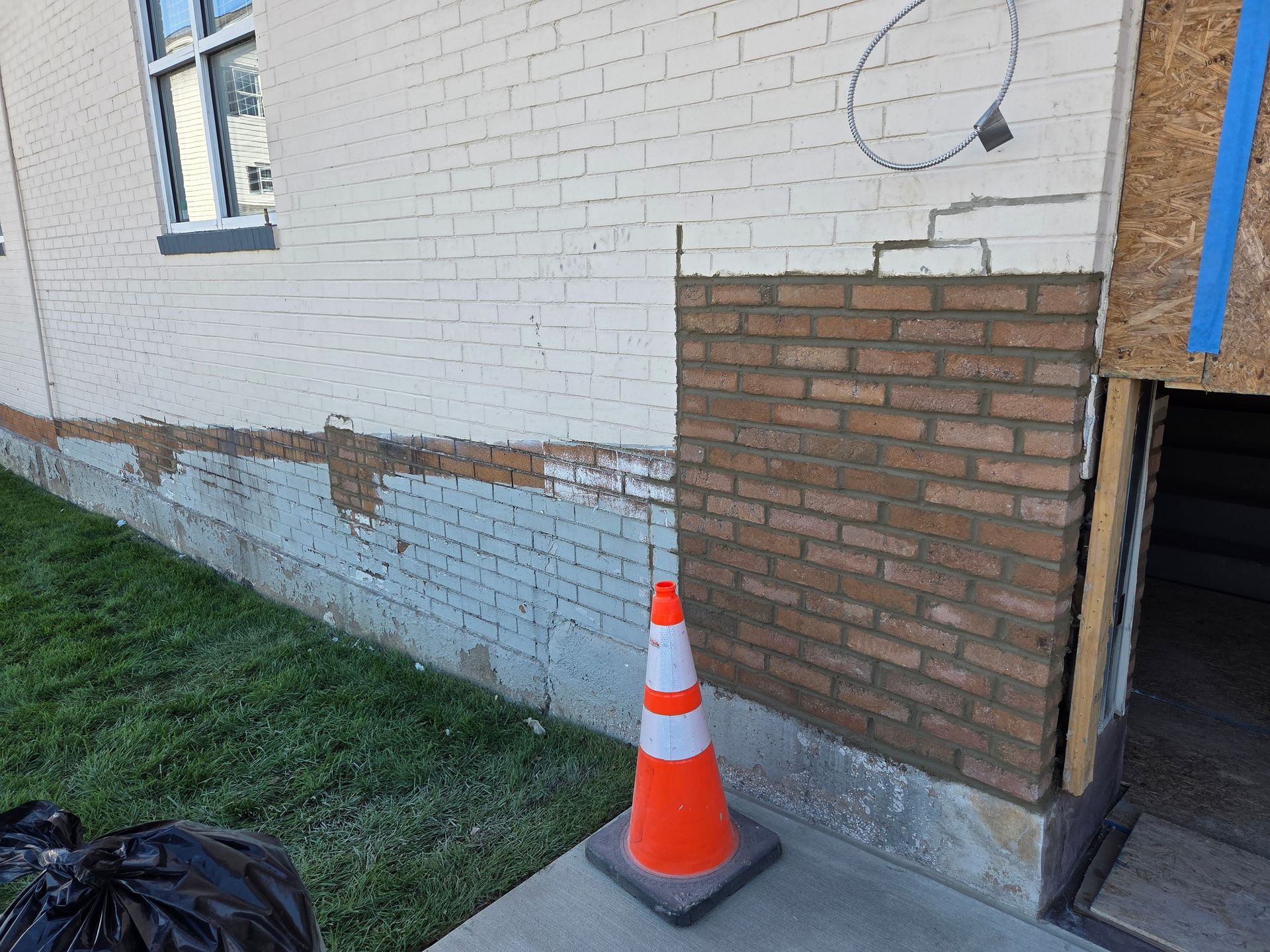 Exterior brick wall repair in progress; sections of old and new brick, with orange safety cone.