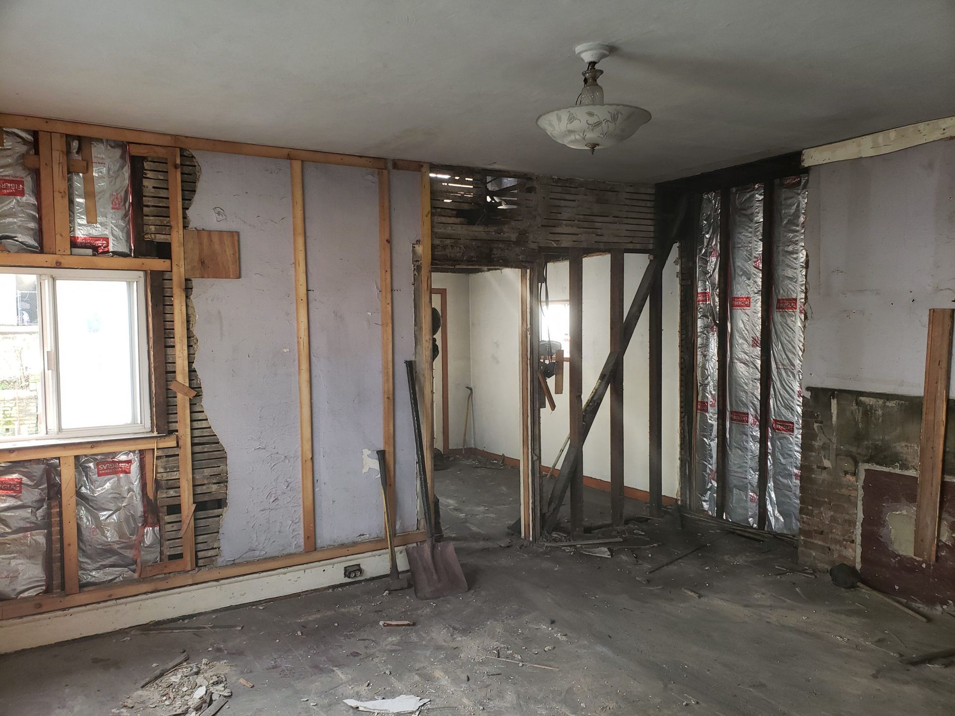 Room under renovation; walls and ceiling partially demolished, insulation exposed, debris on floor.