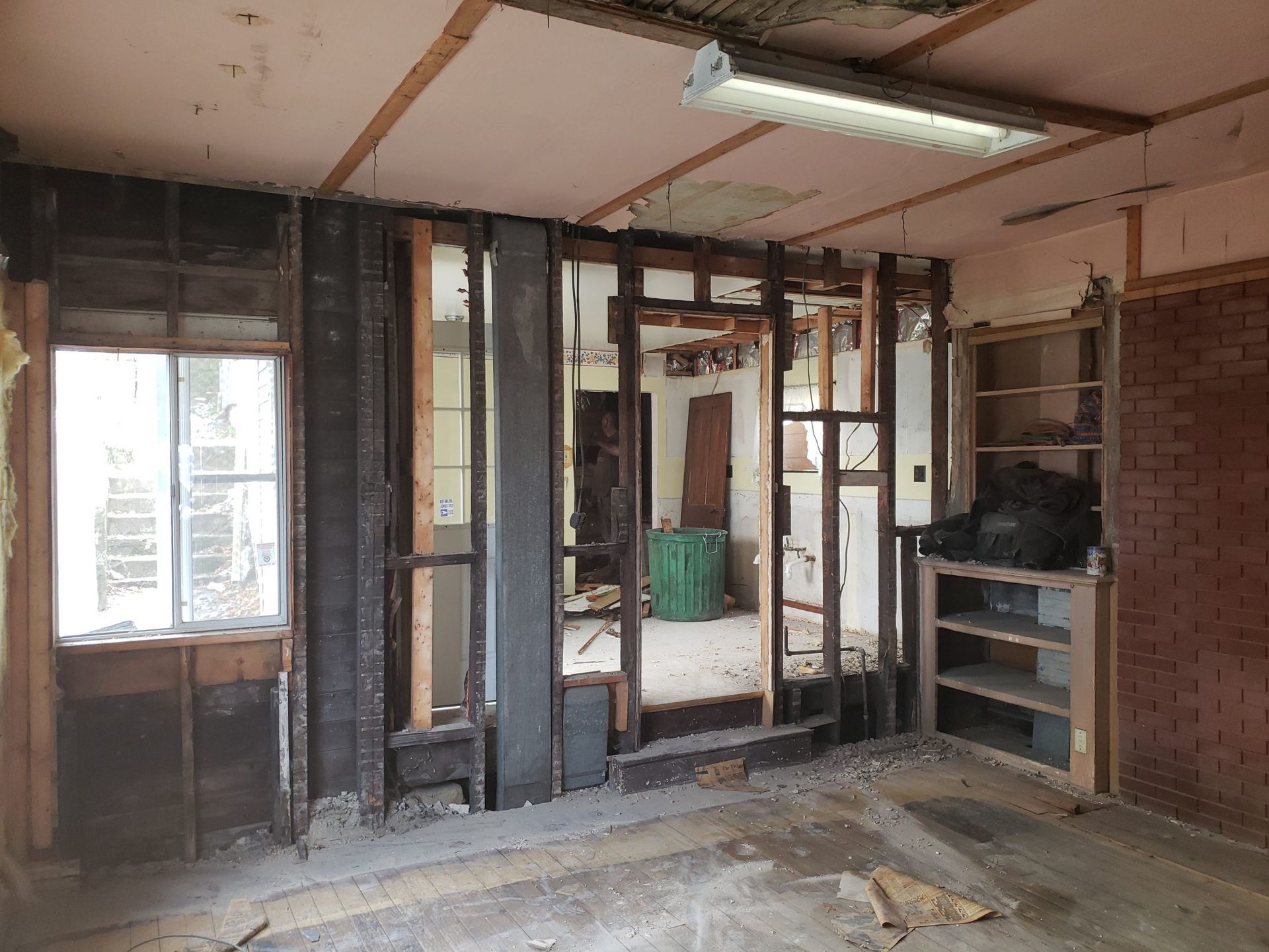 Interior room undergoing renovation; exposed wall studs, window, brick, and shelving.