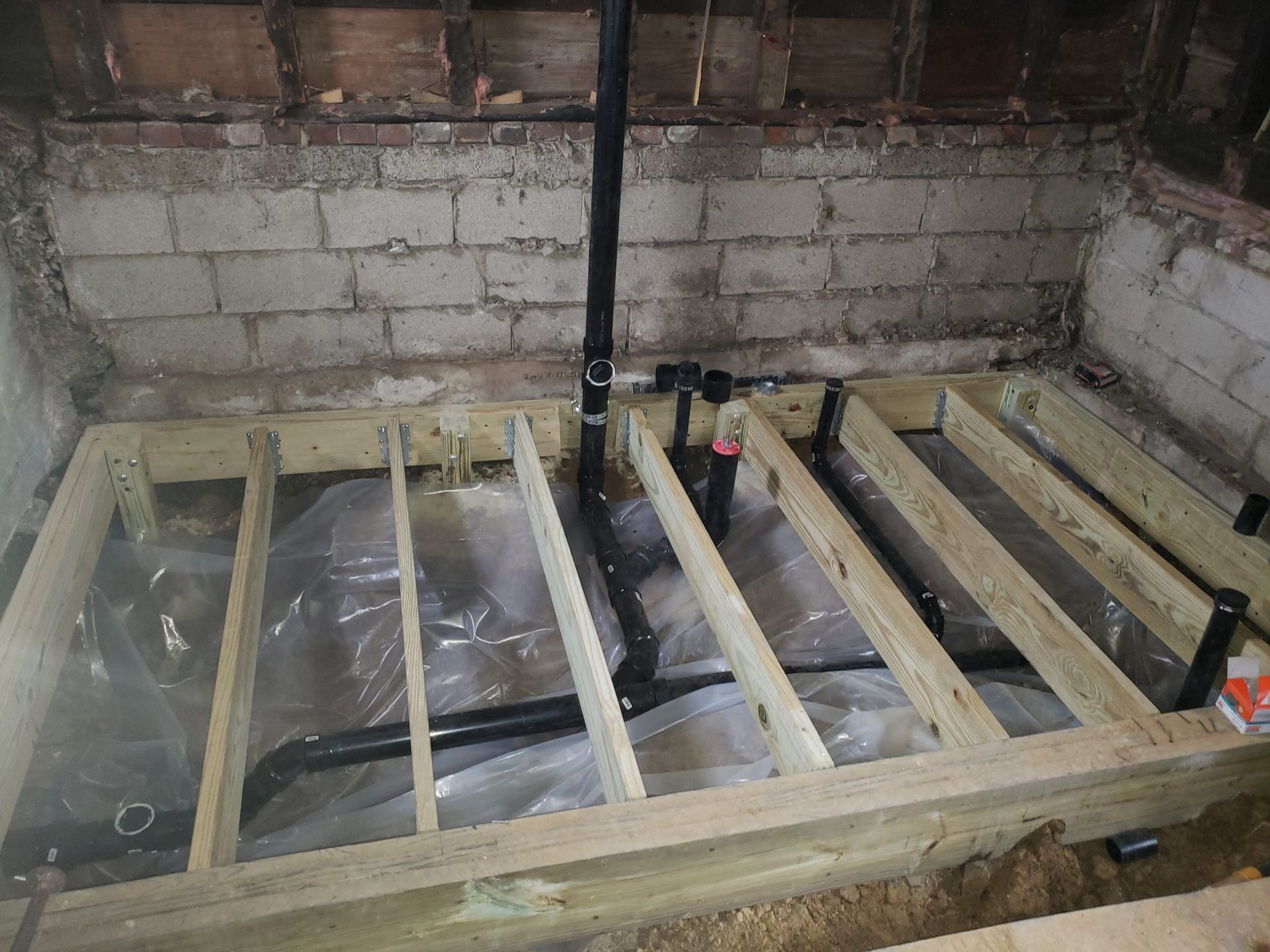 Framed wood flooring under construction, with black plumbing pipes in a basement.