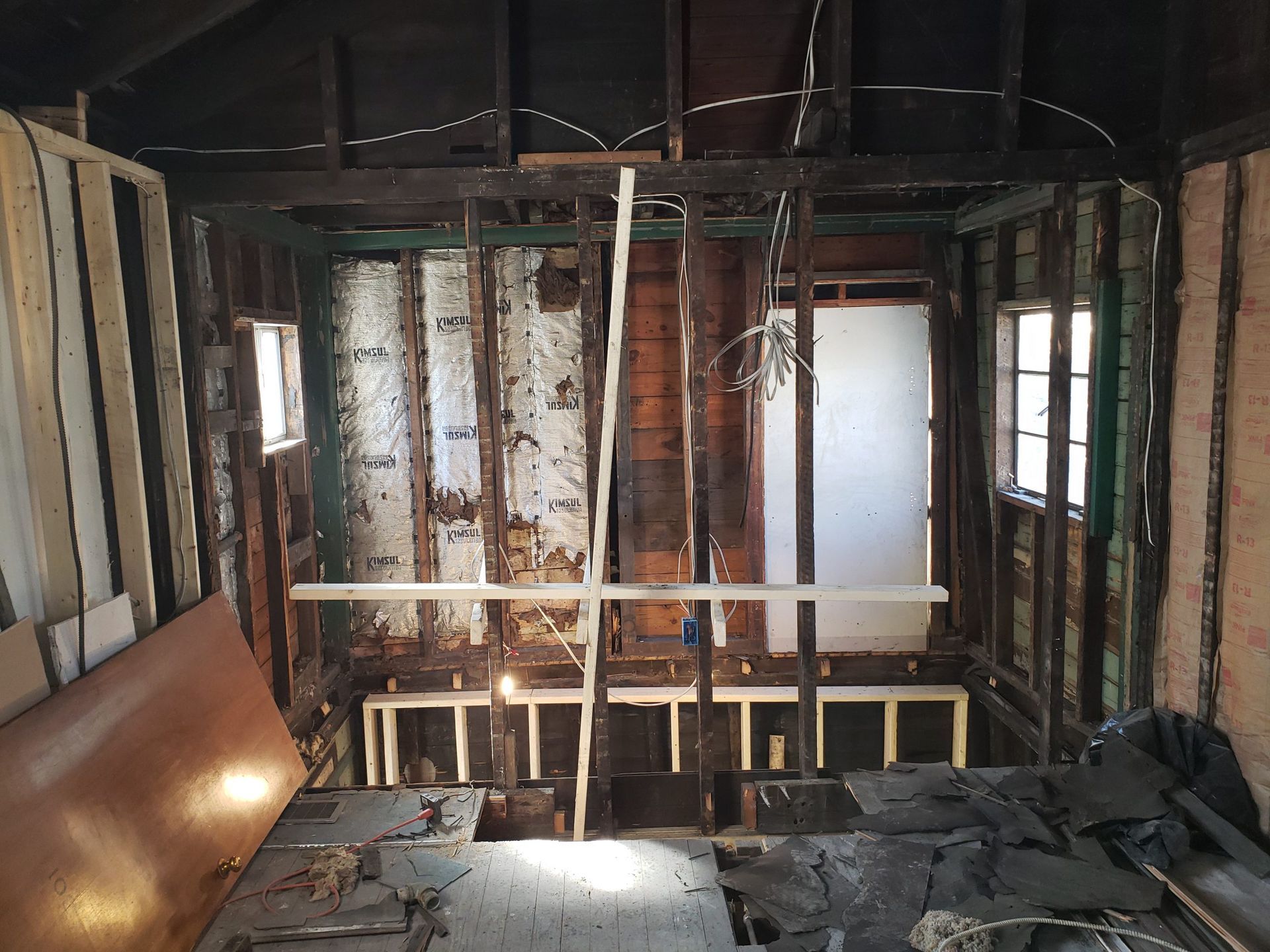 Interior of a building under renovation, showing exposed wooden framing, insulation, and a doorway.